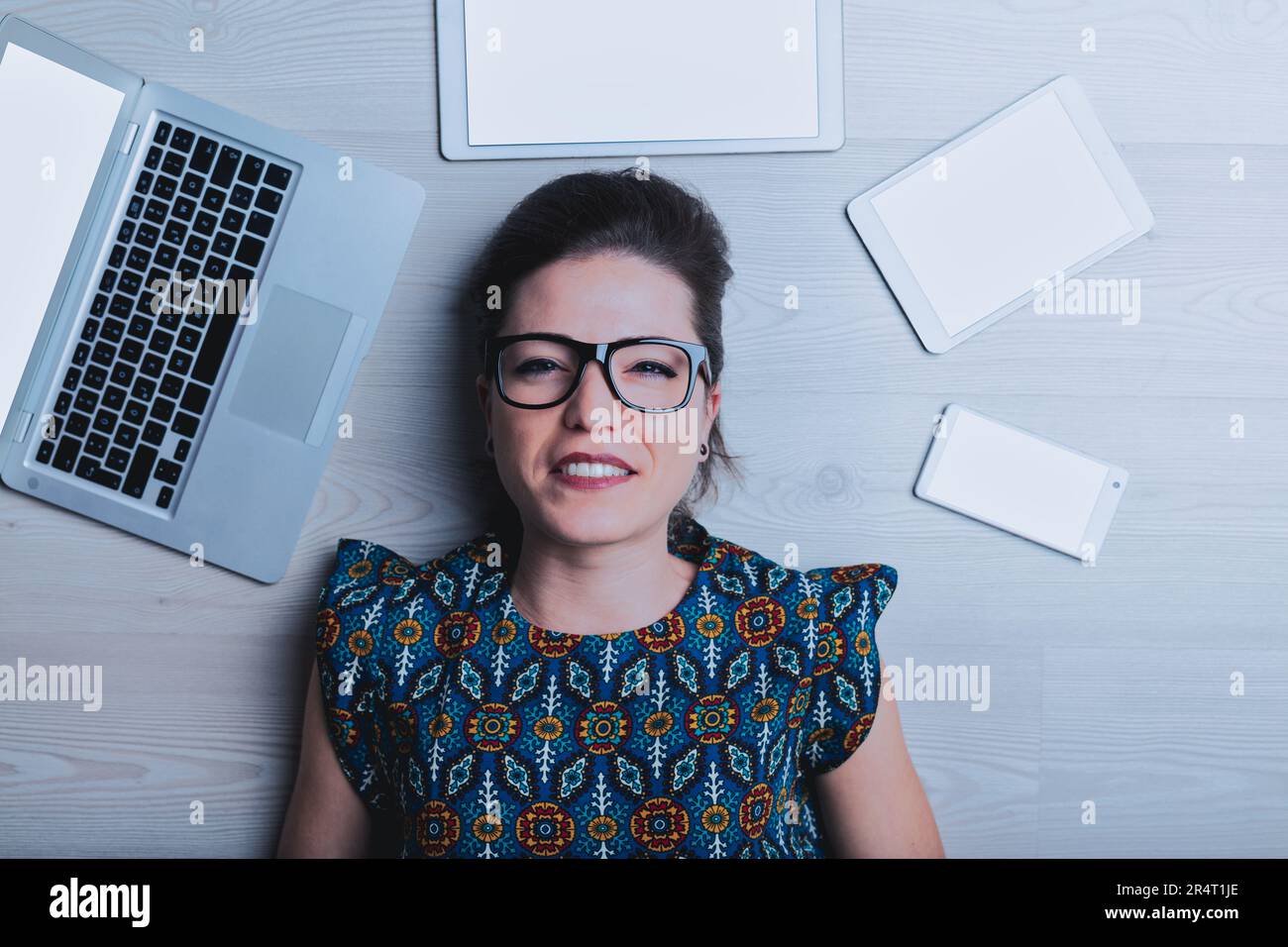 Eine junge Frau, die direkt von oben betrachtet wird, denkt: „Die ganze Technologie widert mich an, ich verstehe gar nichts.“ Ihr Kopf ist von einer verhassten Maschine umgeben Stockfoto