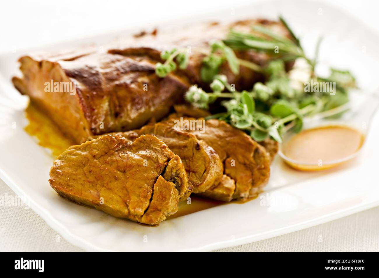 Von oben Stücke von köstlichem Schweinefleisch serviert auf dem Teller zum Mittagessen mit Kräutern und Sauce Stockfoto
