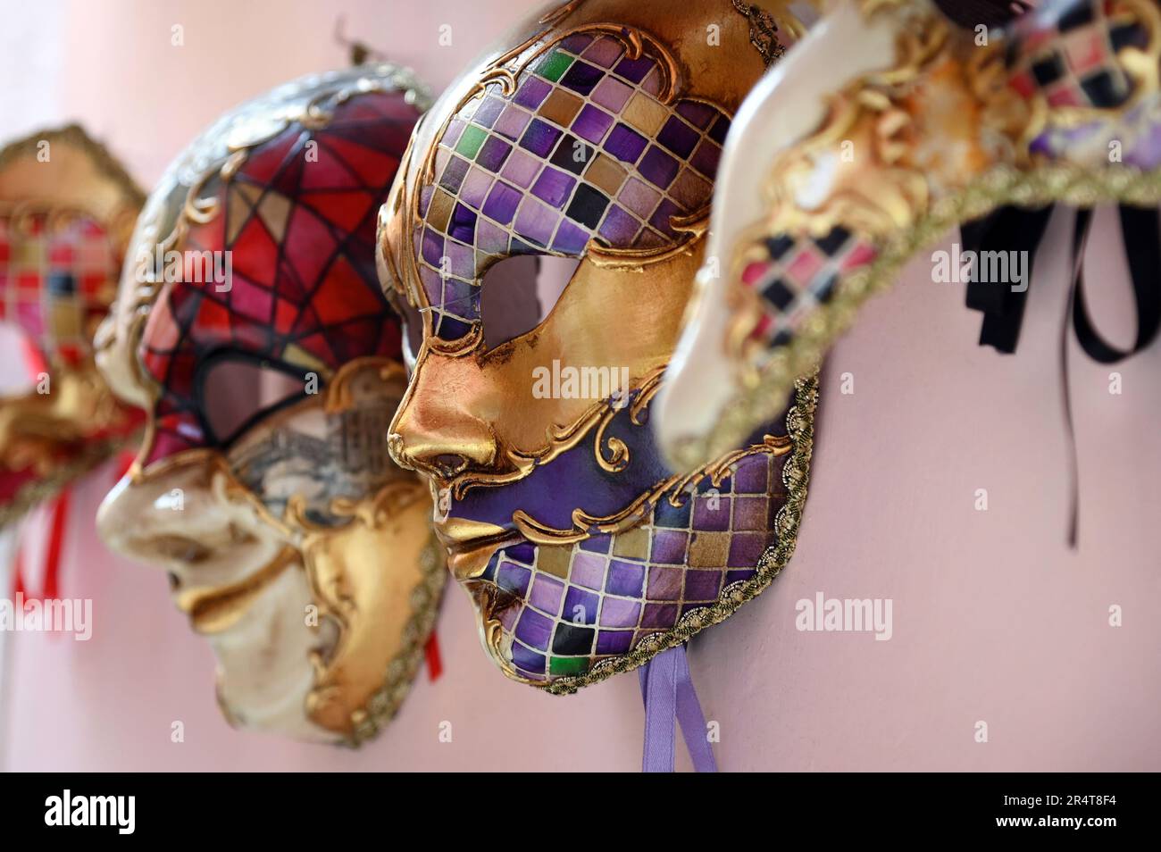 Profilansicht der traditionellen venezianischen Masken für den Karneval, die in Reihe an der rosafarbenen Wand in Venedig, Italien, hängen. Stockfoto