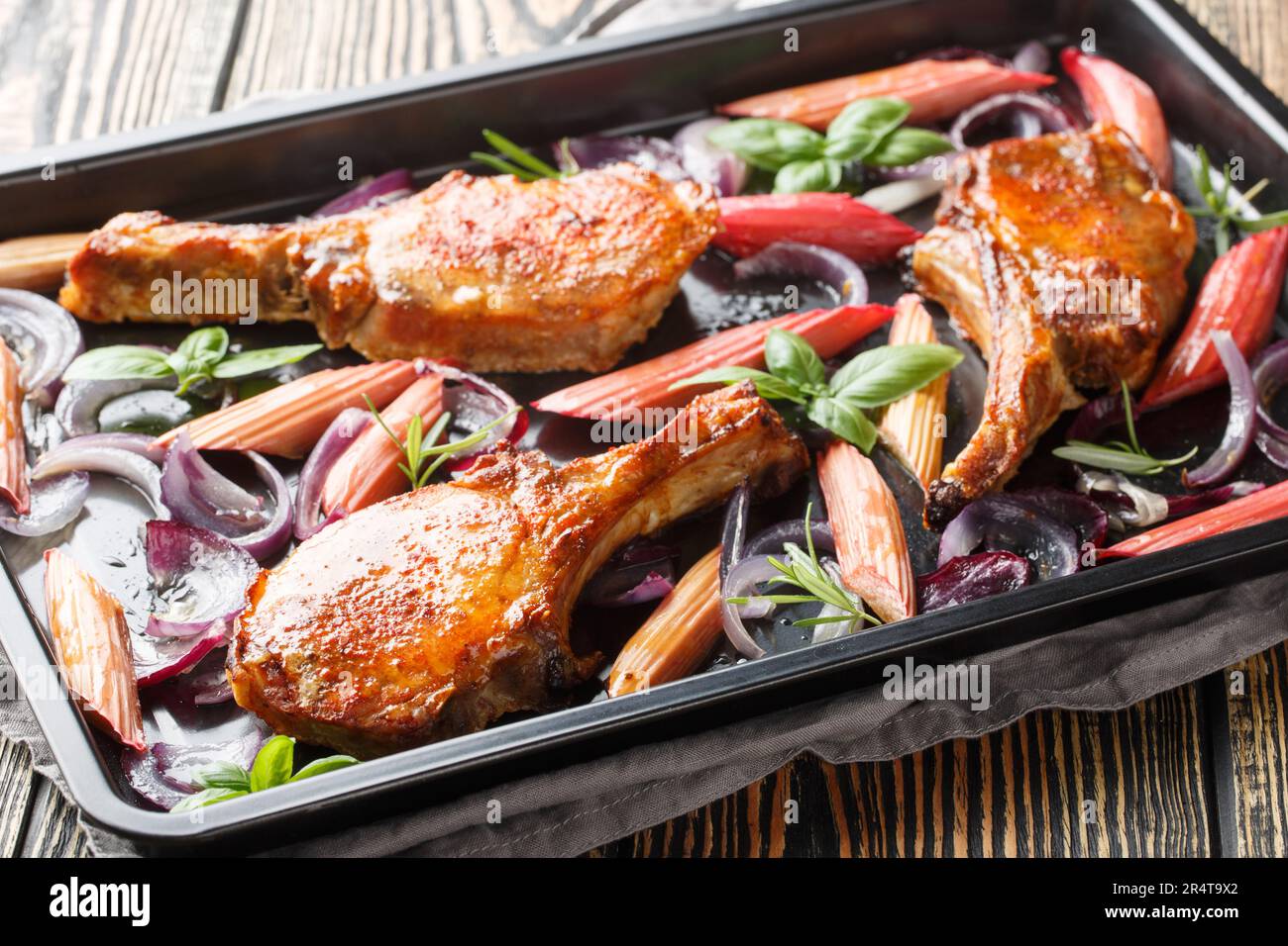 Gebackene Schweinekoteletts mit roten Zwiebeln, Kräutern und Rhabarber in Honigglasur, Nahaufnahme auf einem Backblech auf dem Tisch. Horizontal Stockfoto