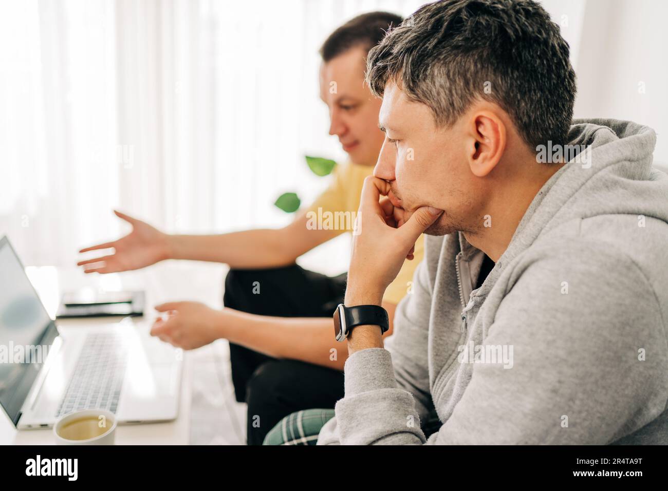 Zwei IT-Freiberufler, die vom Home Office aus ein Notebook eintippen. Zwei Programmierer, die auf der Couch sitzen und Code überprüfen. Fernunterricht online Stockfoto