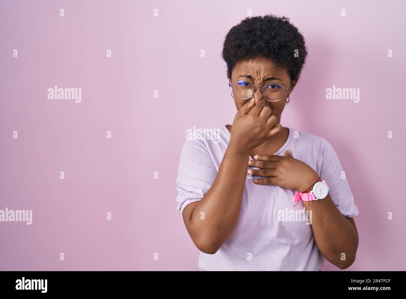 Junge afroamerikanische Frau, die auf rosa Hintergrund steht, riecht etwas stinkendes und