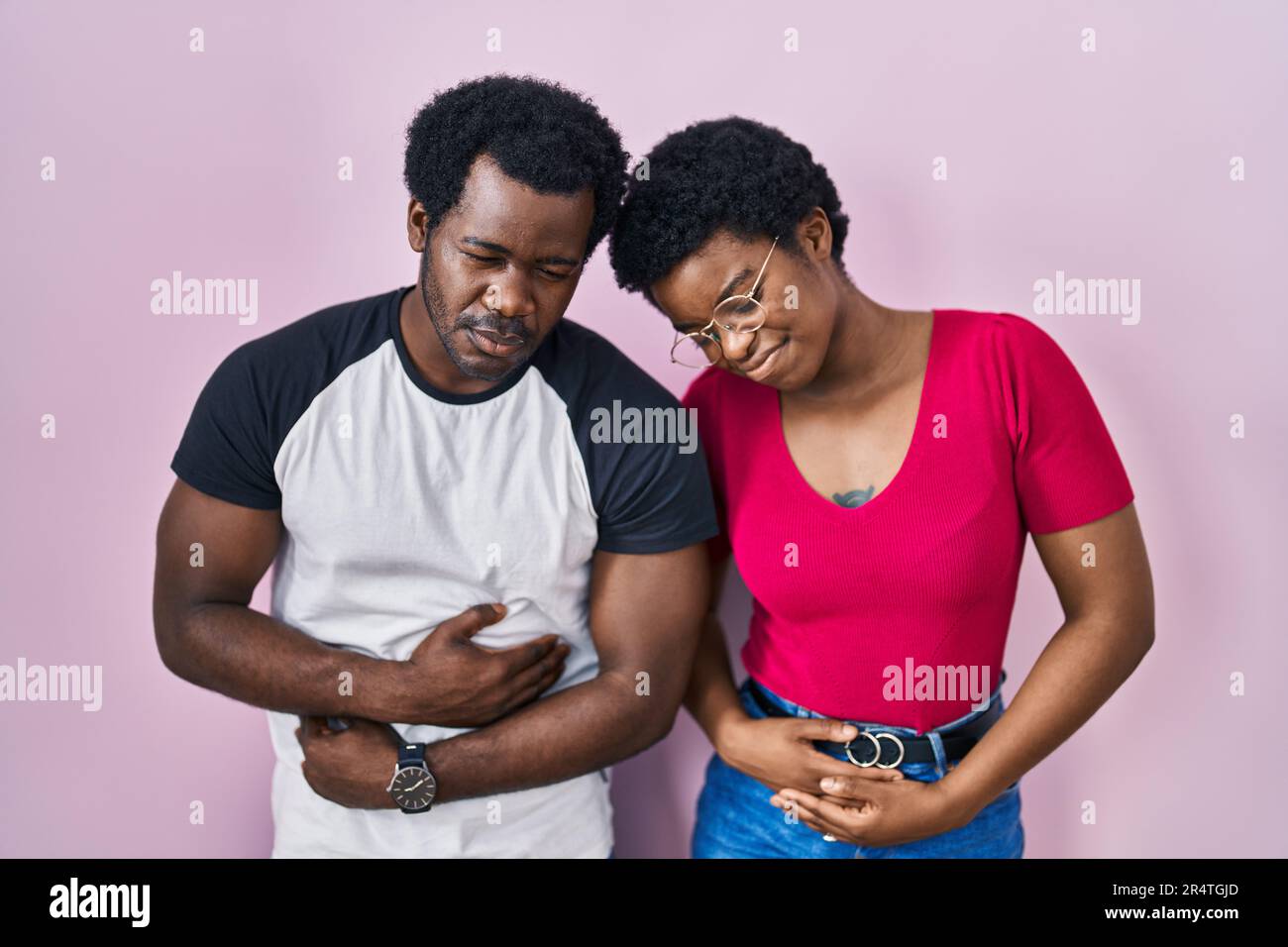 Junges afroamerikanisches Paar, das über rosa Hintergrund steht, mit Hand auf Bauch, weil Verdauungsstörungen, schmerzhafte Krankheit sich unwohl fühlt. Ache-Konzept. Stockfoto