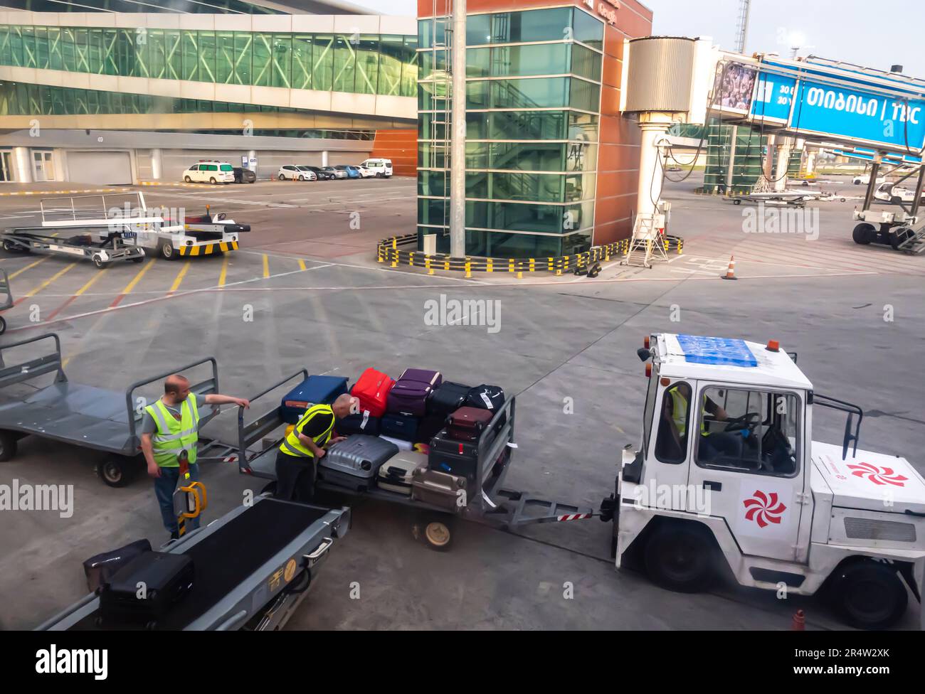 Flughafenmitarbeiter laden Gepäck aus einem Flugzeug in ein Gepäckfahrzeug. Flughafen Tiflis, Georgia. Flughafen Frachtwaggons, Gepäcktraktoranhänger Stockfoto