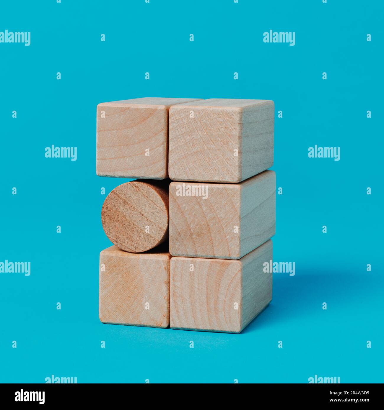 Ein zylindrischer Spielzeugblock in einem Stapel rechteckiger Spielzeugblöcke auf blauem Hintergrund im quadratischen Format Stockfoto
