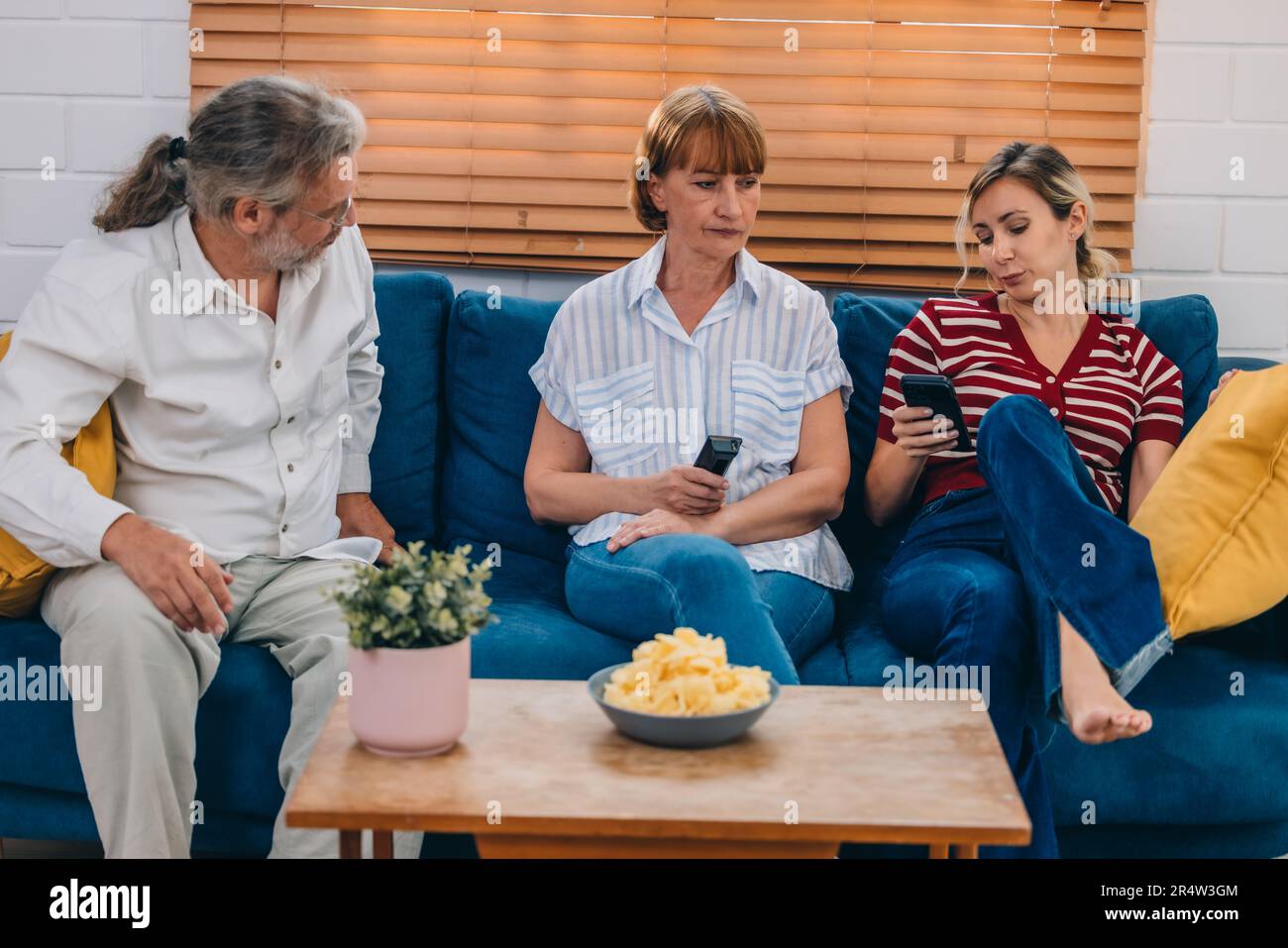 Familienmitglieder aus mehreren Generationen genießen eine schöne Zeit zusammen, indem sie Fernsehen, Snacks und Gespräche teilen und neue entdecken Stockfoto