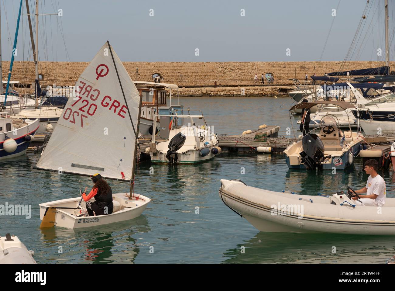 Heraklion, Kreta, Griechenland, Europa. 2023. Junges Mädchen auf einer Segelstunde in einem Schlauchboot im alten Hafen, beobachtet vom Lehrer im Hafen, Stockfoto