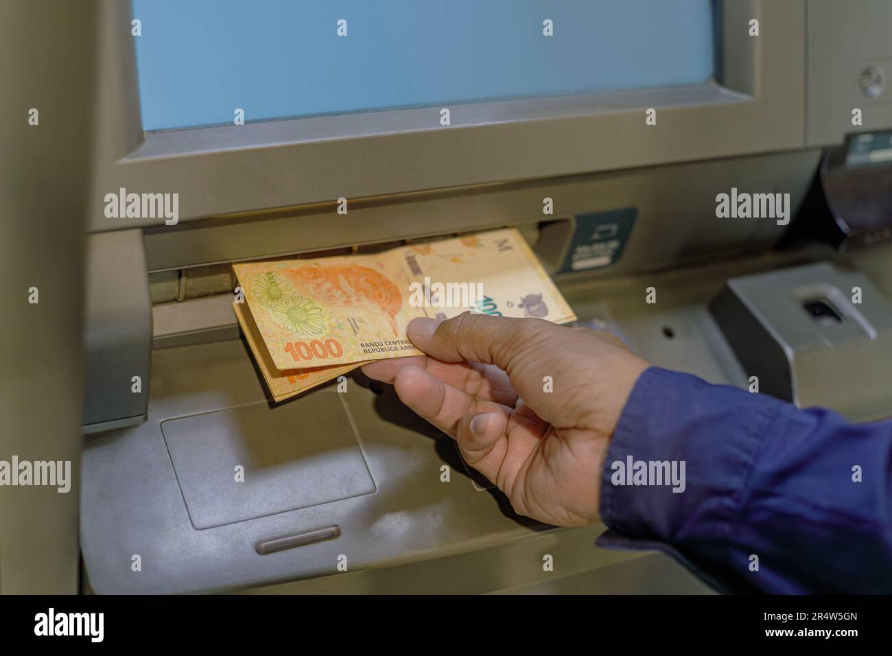 Detail einer Hand, die argentinische Pesos-Scheine aus einem Geldautomaten holt. Stockfoto