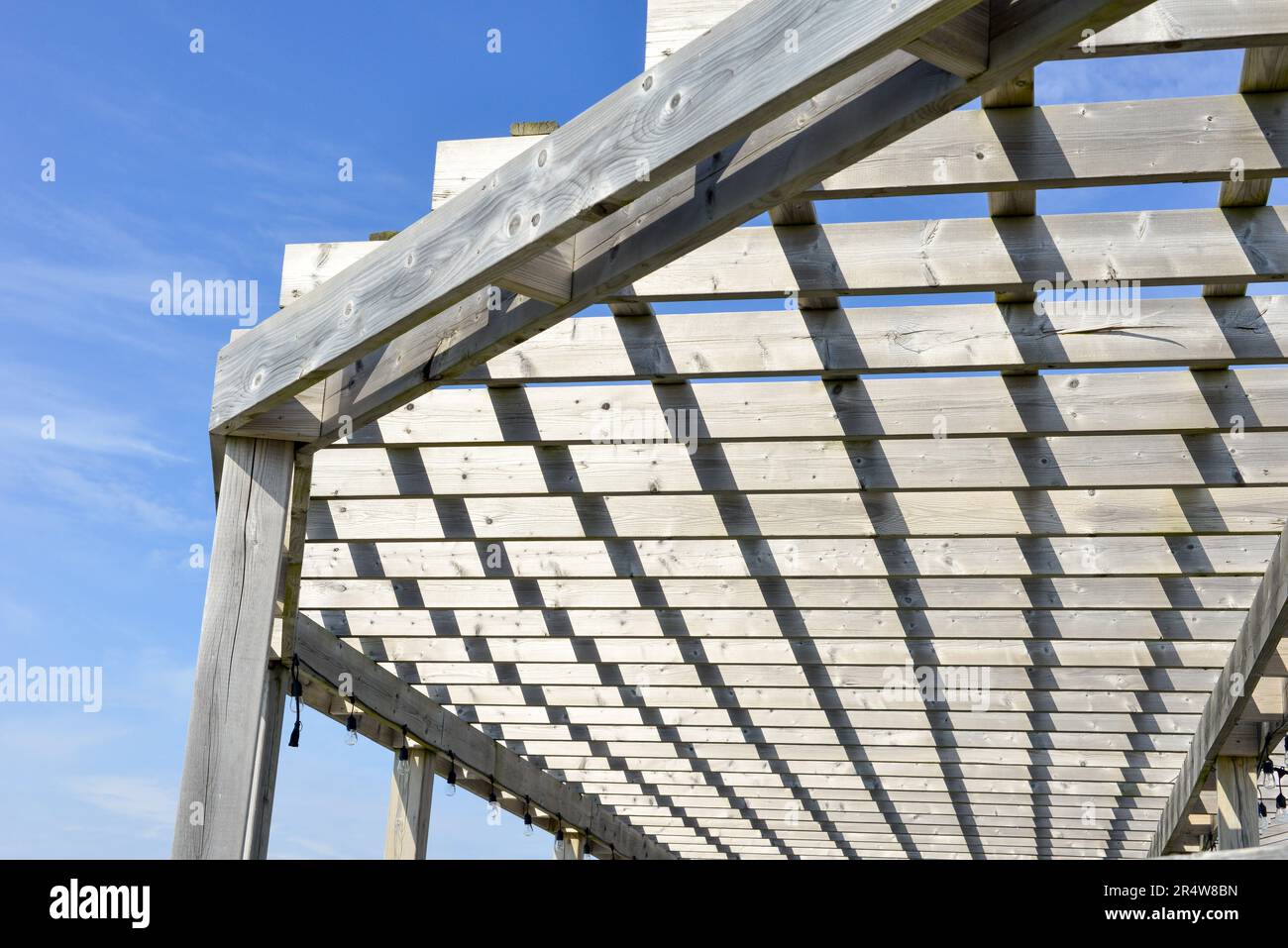 Ein grau abgenutztes und verwittertes Dach aus Holzpergola mit blauem Himmel im Hintergrund. Der Sonnenschutz im Freien hat Holzlatten, die über dem Holz hängen Stockfoto