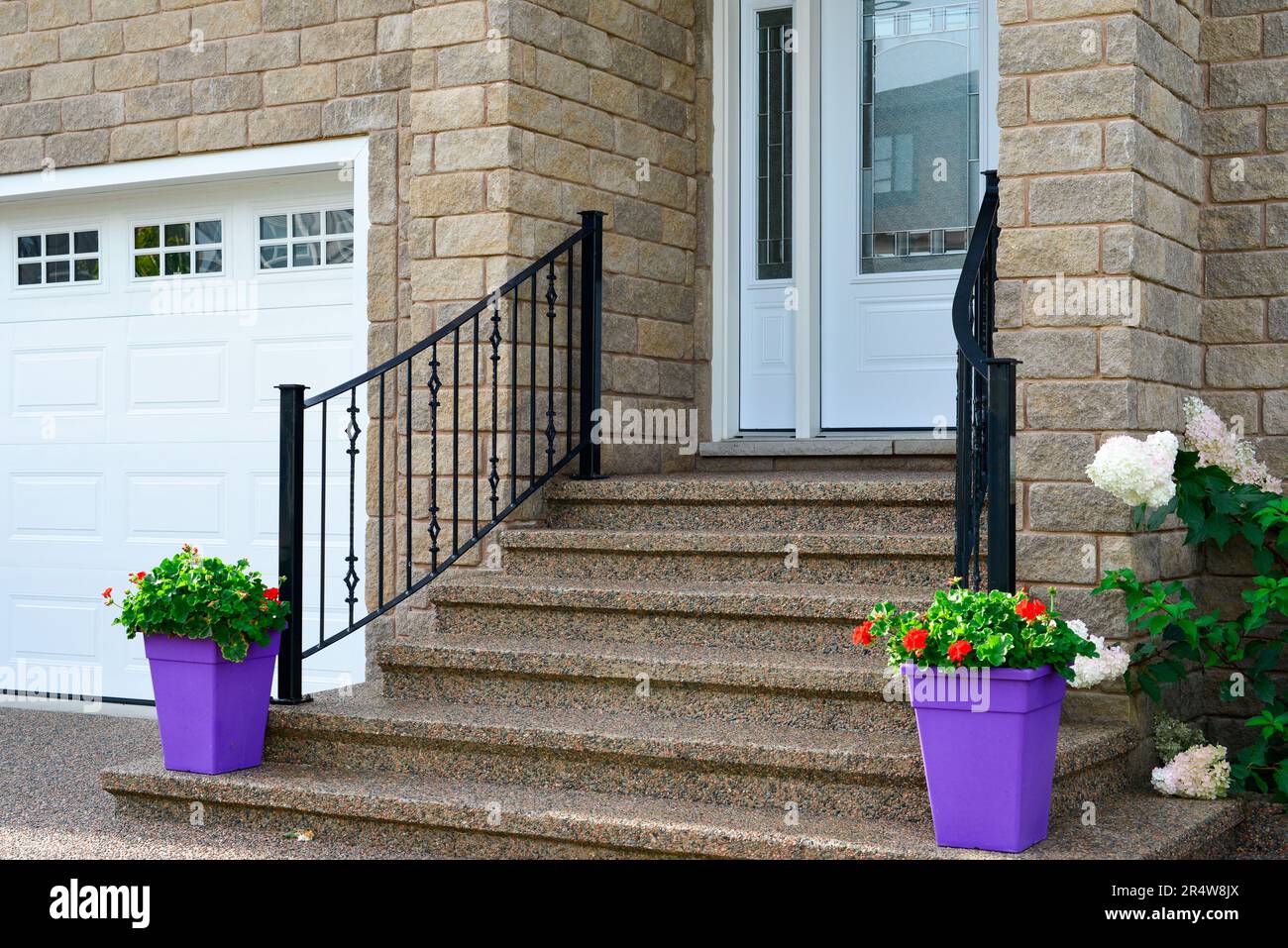 Eine große weiße Garagentür mit kleinen Glasfenstern in einem beigen Ziegelgebäude mit einer weißen Tür und Stufen, die zu einem großen Eingang führen. Stockfoto