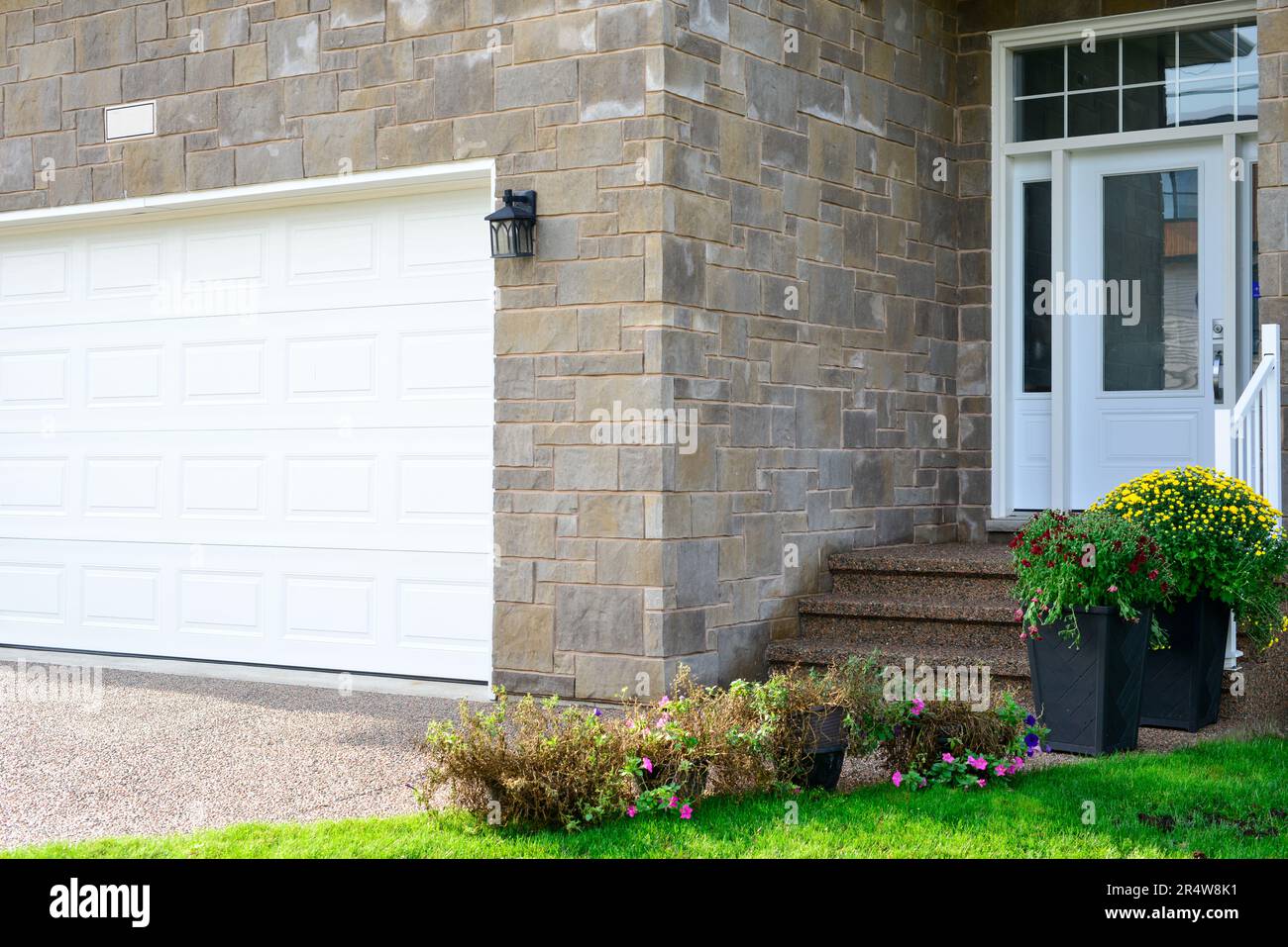 Eine große weiße Garagentür mit kleinen Glasfenstern in einem beigen Ziegelgebäude mit einer weißen Tür und Stufen, die zu einem großen Eingang führen. Stockfoto