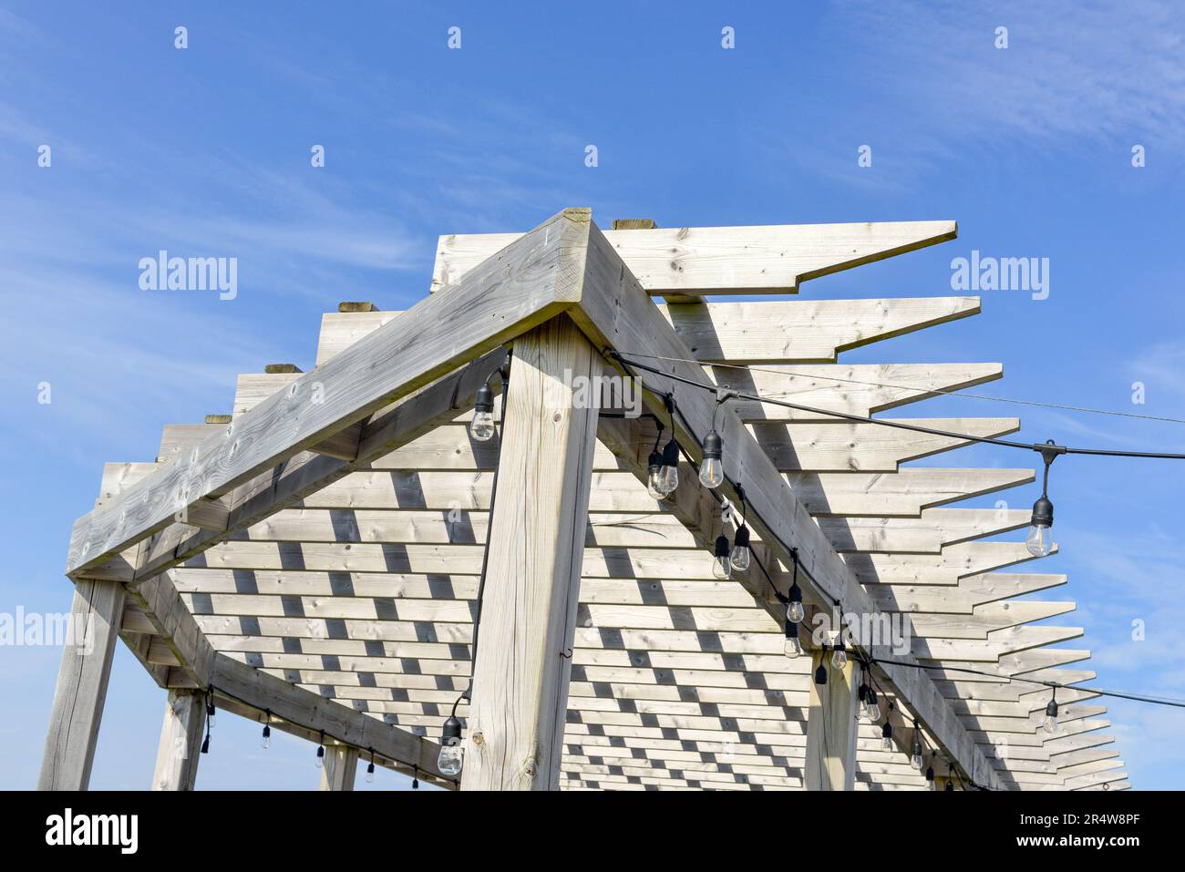 Graues, abgenutztes und verwittertes Dach aus Holzpergola mit blauem Himmel. Der Sonnenschutz im Freien verfügt über Holzleisten in einem Muster mit spitzen Kanten. Stockfoto
