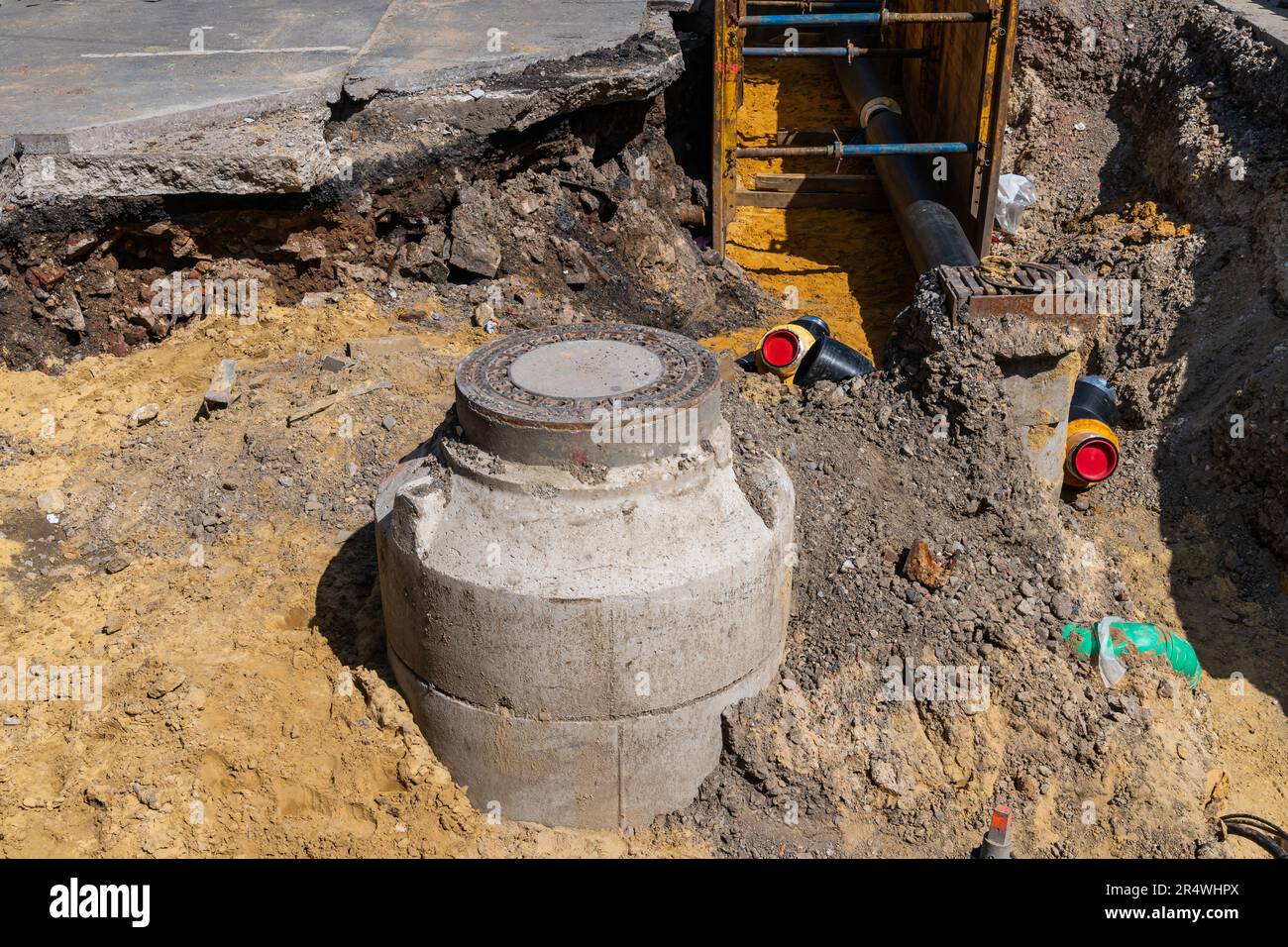 Ein zur Reparatur ausgegrabener Abwasserkanal mit einem Metallschacht und neuen daran angeschlossenen Rohren. Stockfoto