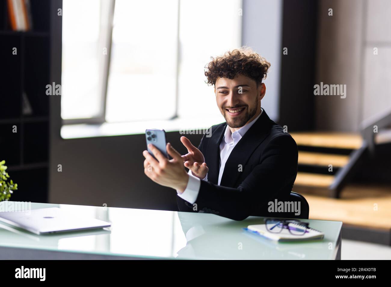 Junger weißer Angestellter, der Videoanrufe über ein Smartphone führt, während er im Büro sitzt. Stockfoto