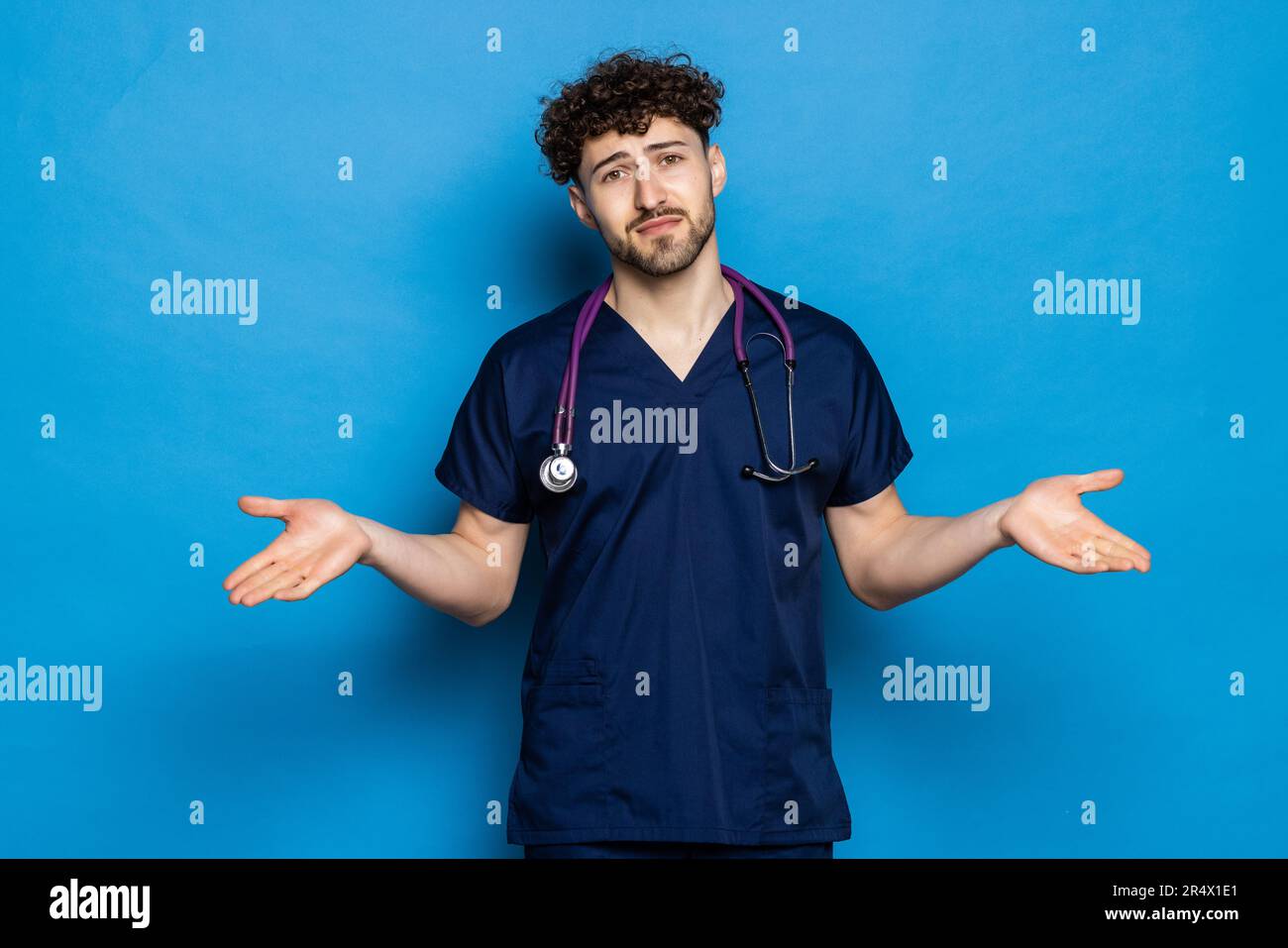 Junger gutaussehender Arzt mit Bart, der Mantel und Brille über blauem Hintergrund trägt, verwirrt und fragt sich nach der Frage. Unsicher mit Zweifel, denken w Stockfoto