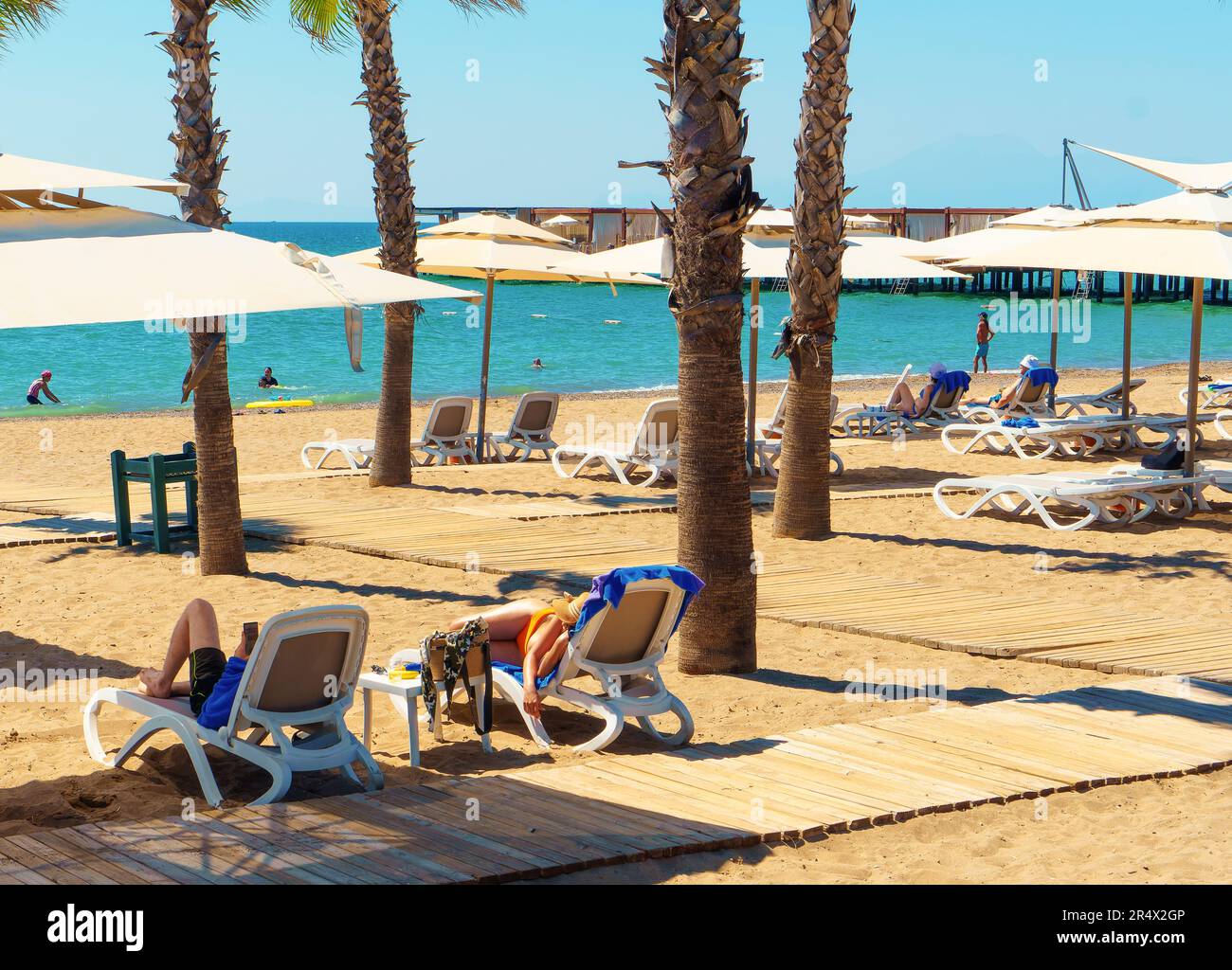 Antalya; Türkei-September 10; 2022: Touristenpaar ruht sich auf Liegen aus und sonnt sich unter Palmen am Strand. Die Leute schwimmen im Meer Stockfoto