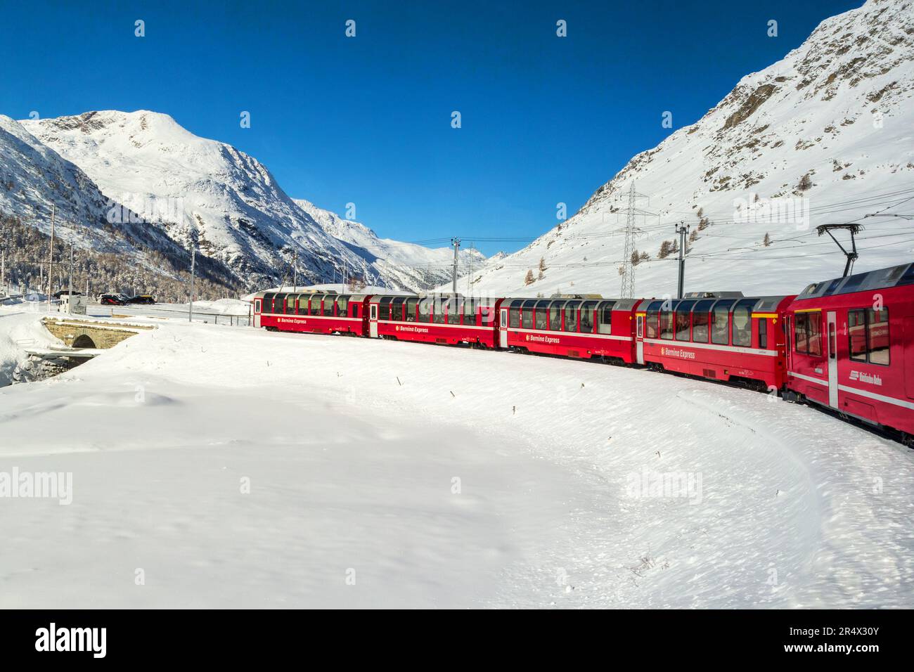 Grisons, Schweiz - November 05. 2021 Uhr: Der berühmte rote Bernina Express Touristenzug überquert das Schneefeld in der Höhe der Alpen. Stockfoto