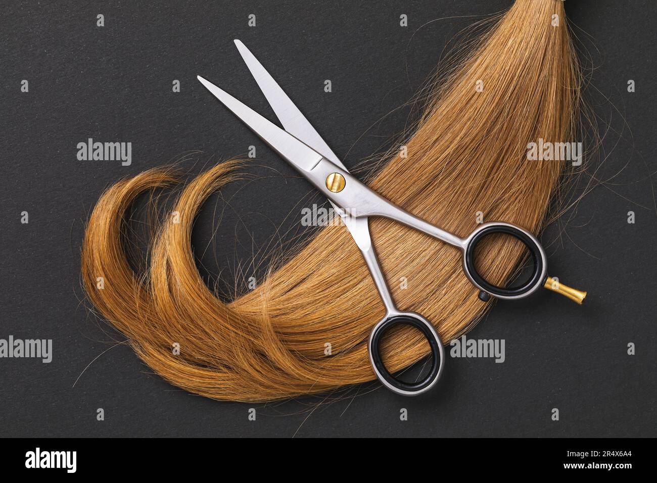 Schere zum Schneiden von Haaren und eine abgeschnittene Strähne blonder Kinderhaare auf dunklem Papierhintergrund Stockfoto