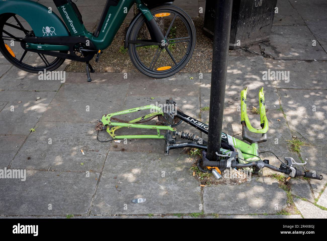 Der Rahmen eines entsorgten und verlassenen Fahrrads bleibt am 23. Mai 2023 in London, England, neben einem Leihfahrrad in Southwark, Süd-London, an einem Pfosten befestigt. Stockfoto