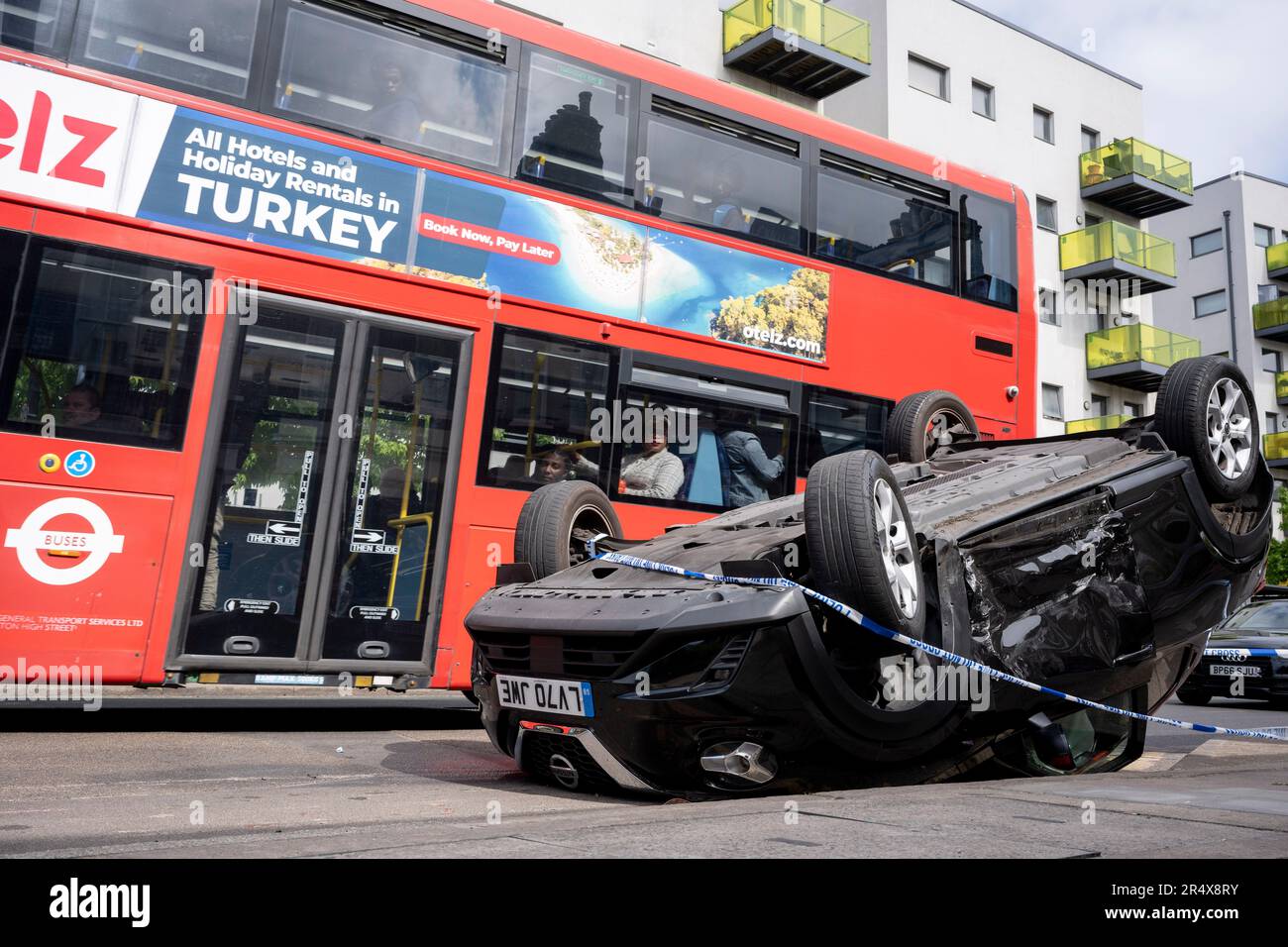 Ein Londoner Bus passiert die Folgen eines Autounfalls, bei dem am 30. Mai 2023 in London, England, ein umgestürzter Nissan-Heck am Straßenrand zwischen Brixton und Camberwell auf der Coldharbour Lane verbleibt. Stockfoto