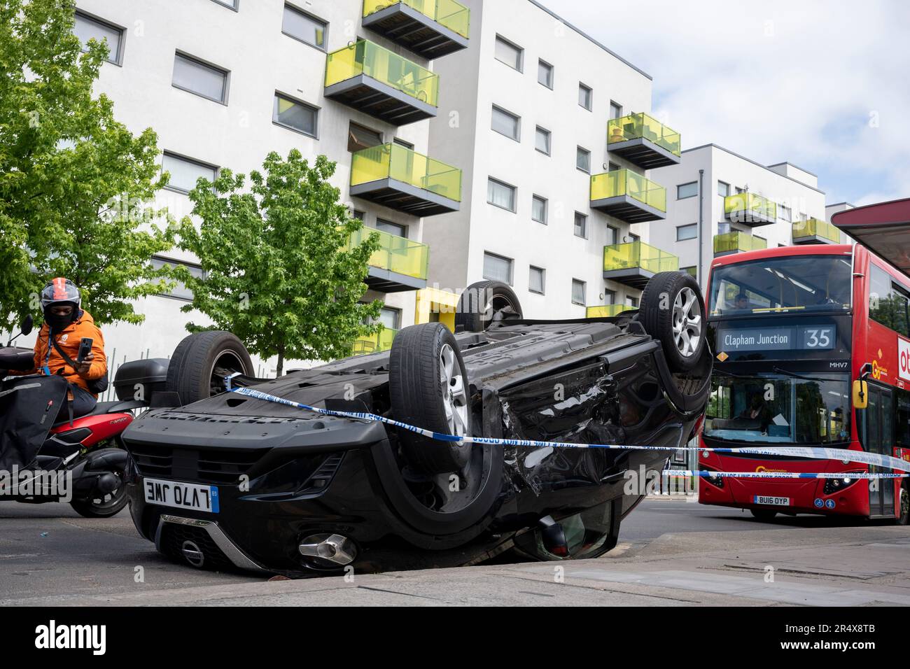 Ein Bus nähert sich den Folgen eines Autounfalls, bei dem am 30. Mai 2023 in London, England, ein umgestürzter Nissan-Heck am Straßenrand zwischen Brixton und Camberwell auf der Coldharbour Lane verbleibt. Stockfoto