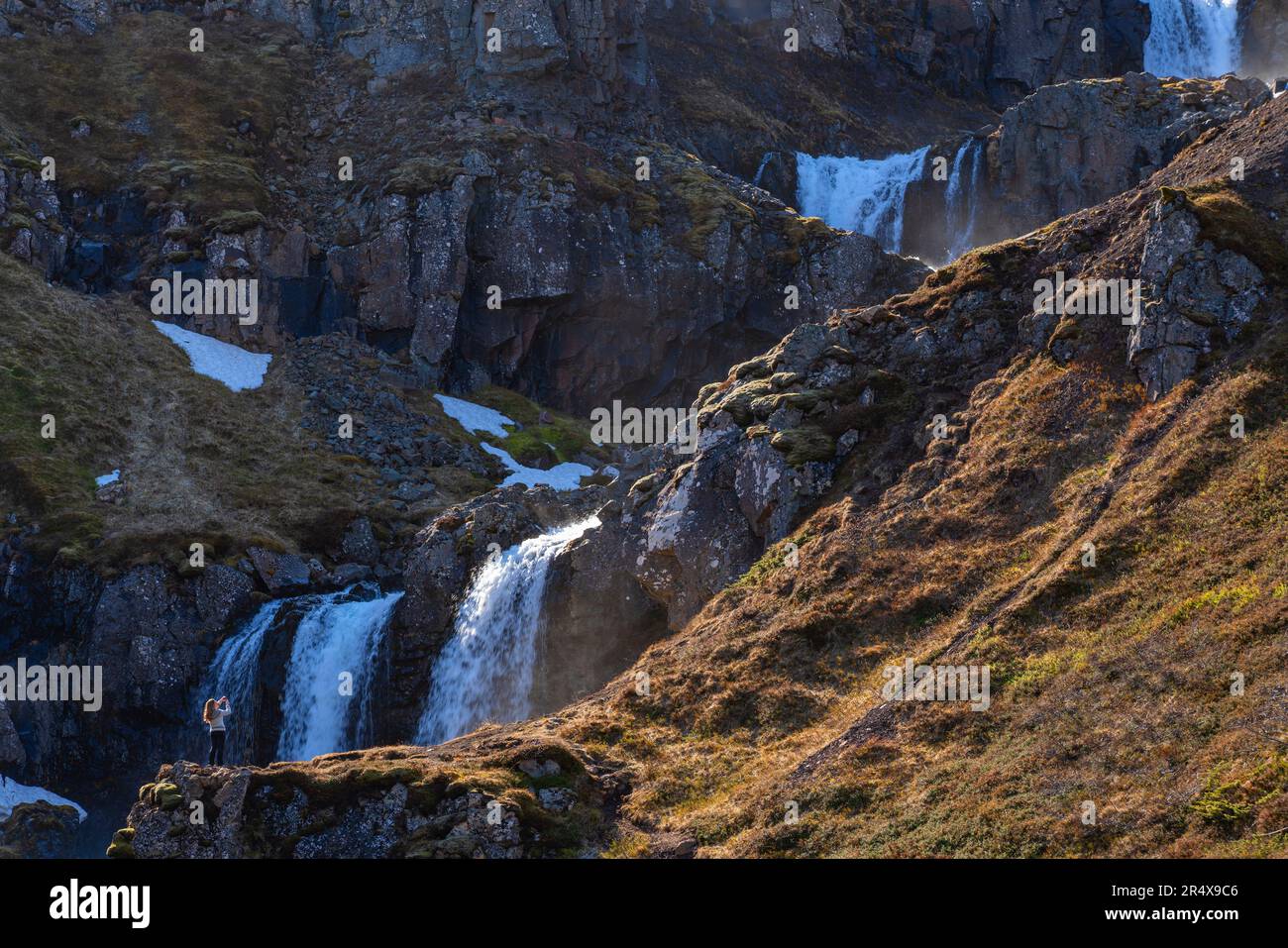 Malerischer Blick auf eine Frau, die mit ihrem Smartphone ein Foto macht, auf einem Klippenhang vor einer Reihe von Wasserfällen, die aus dem cr fließen... Stockfoto