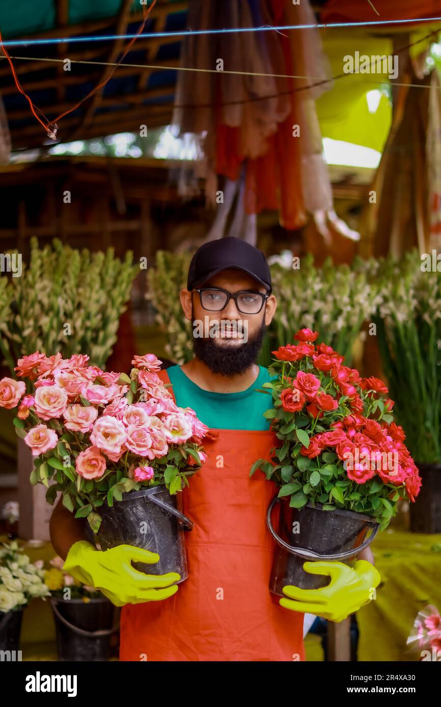 Arbeiter im Blumenladen, Porträt eines wunderschönen Mannes, der während der Arbeit in einem Gewächshaus steht, lächelnd erfolgreiche junge Pflanze. Stockfoto