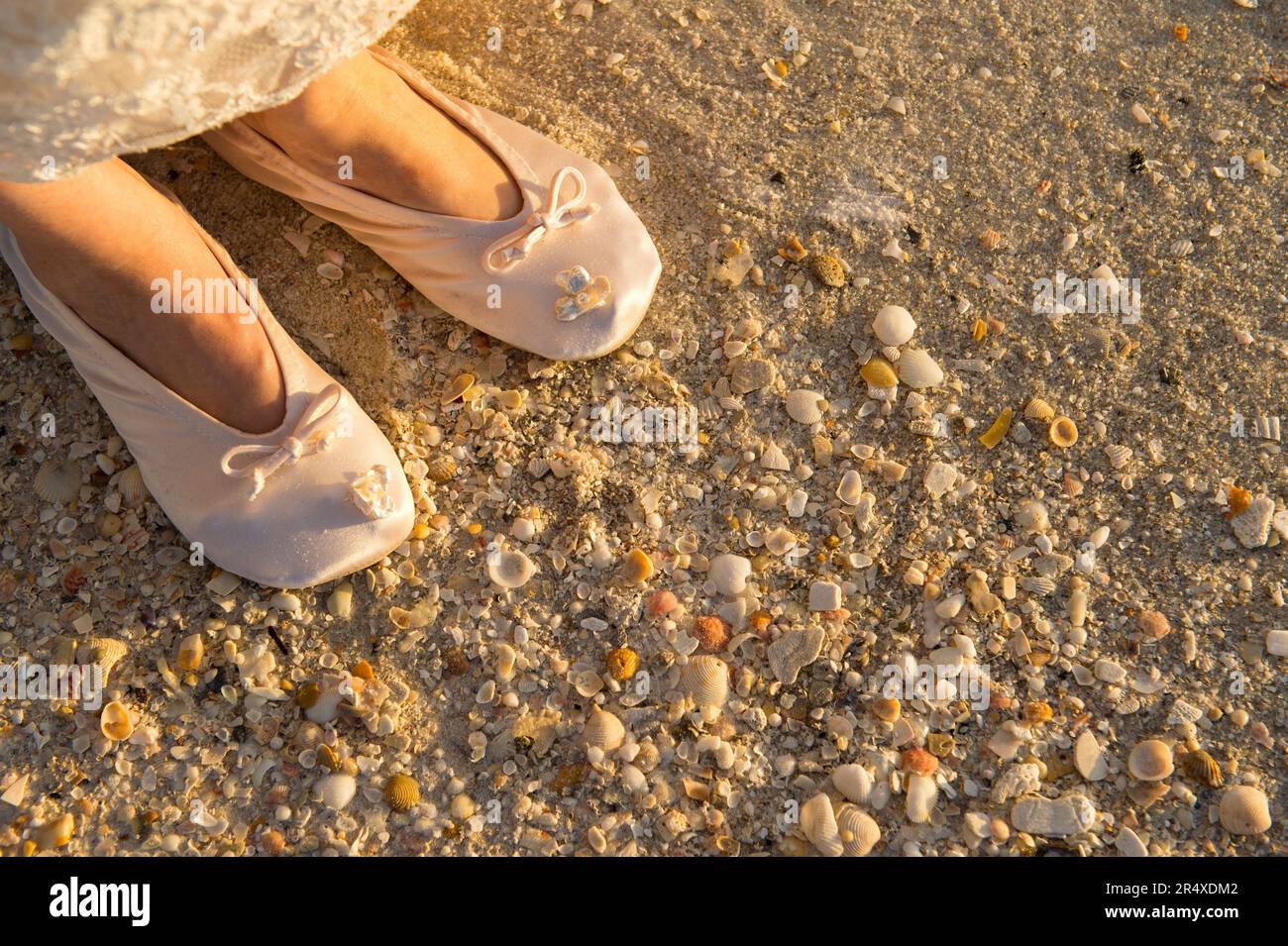 Eine Frau in ihren Hochzeitspantoffeln steht an einem muschelüberdachten Strand; Panama City Beach, Florida, Vereinigte Staaten von Amerika Stockfoto