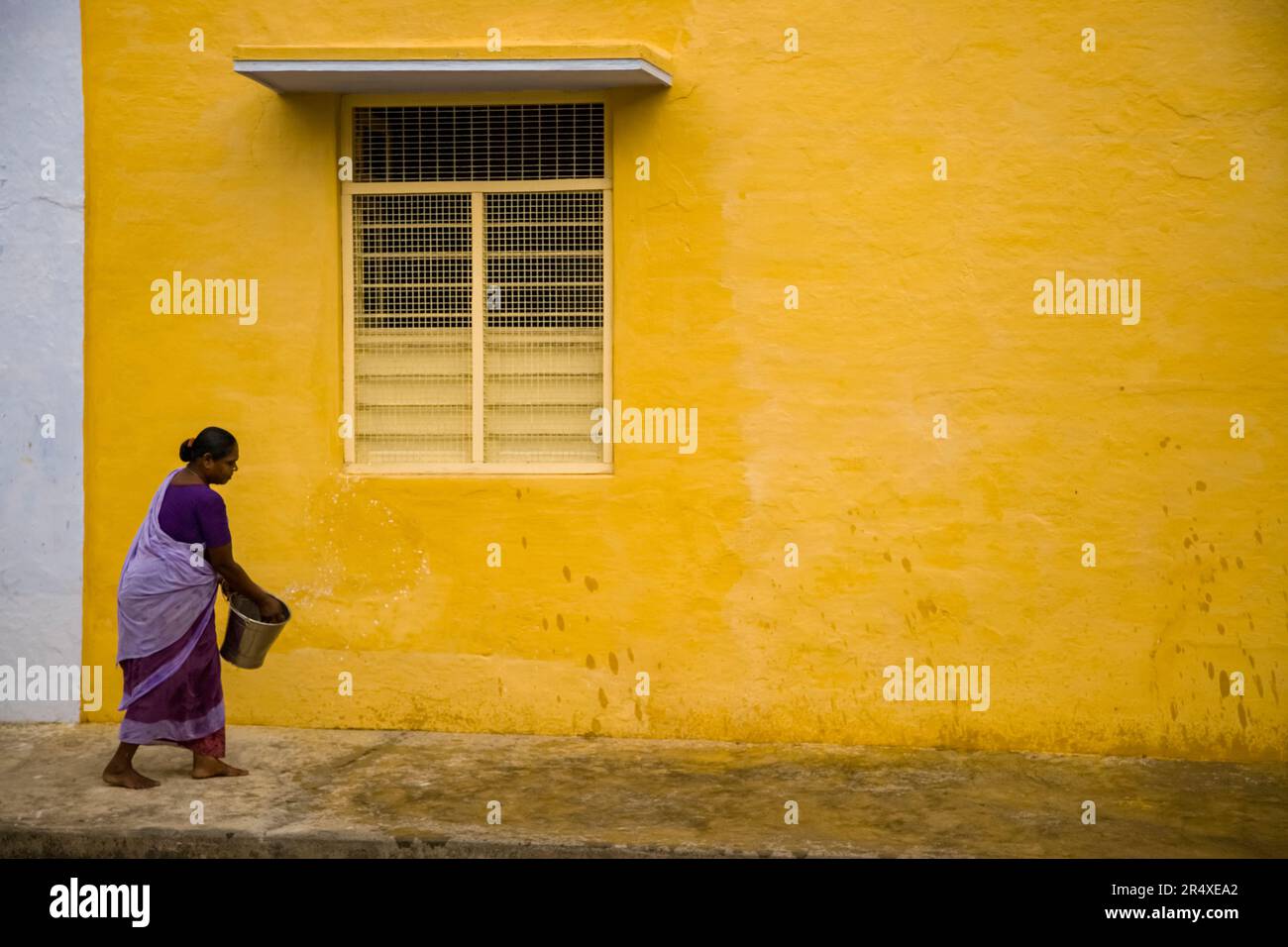 Frau bewässert einen unbefestigten Bürgersteig in Indien; Puducherry, Tamil Nadu, Indien Stockfoto