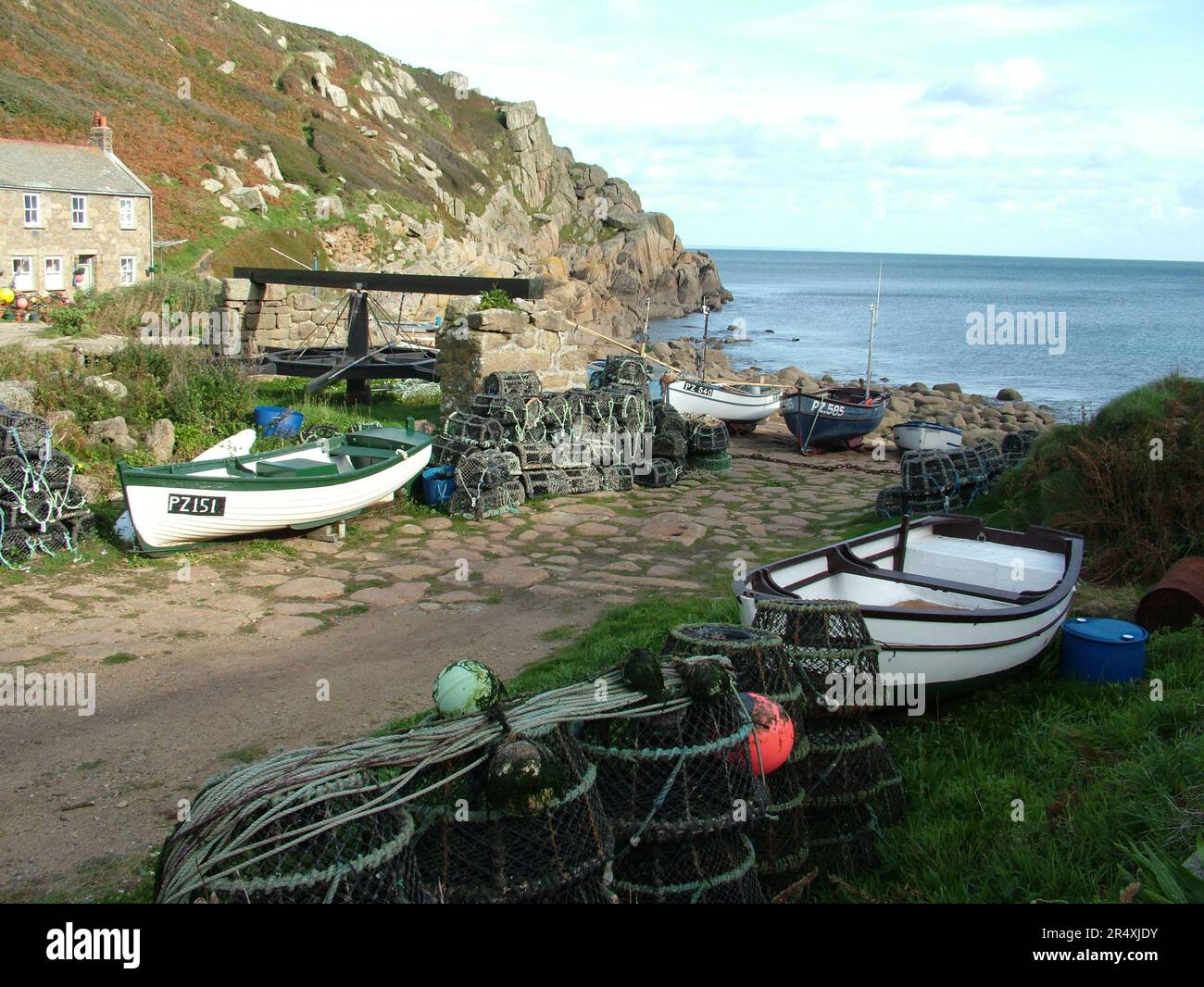 Die alte Seilwinde mit Krabben- und Hummertöpfen und Fischerbooten über der Hellbahn am Penberth Cove Harbour, Cornwall, England, Großbritannien. Stockfoto