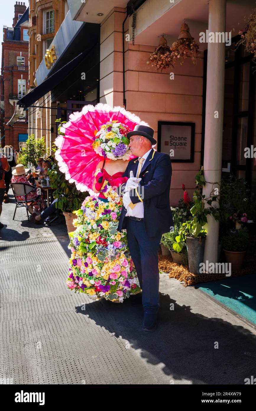 Eine Frau, die ein aufwändiges, farbenfrohes Kleid mit Blumenmuster trägt und einen roten Sonnenschirm am Sloane Square Hotel, Chelsea, London SW1 während Chelsea in Bloom trägt Stockfoto