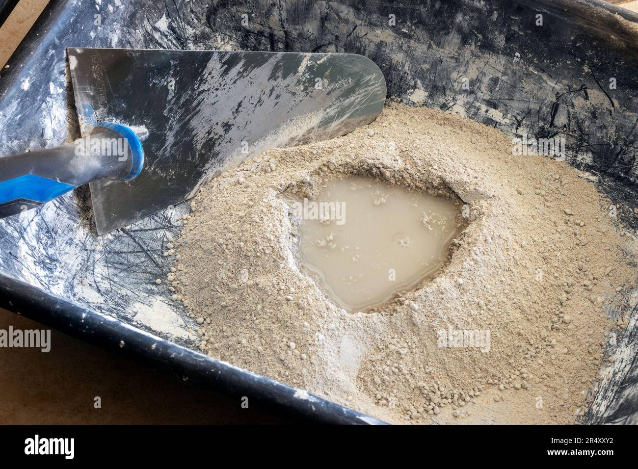 Zementpulver mit Wasser, fertig zur Mischung mit einer Kelle in einer Kunststoffschüssel, Mörtelherstellung. Stockfoto