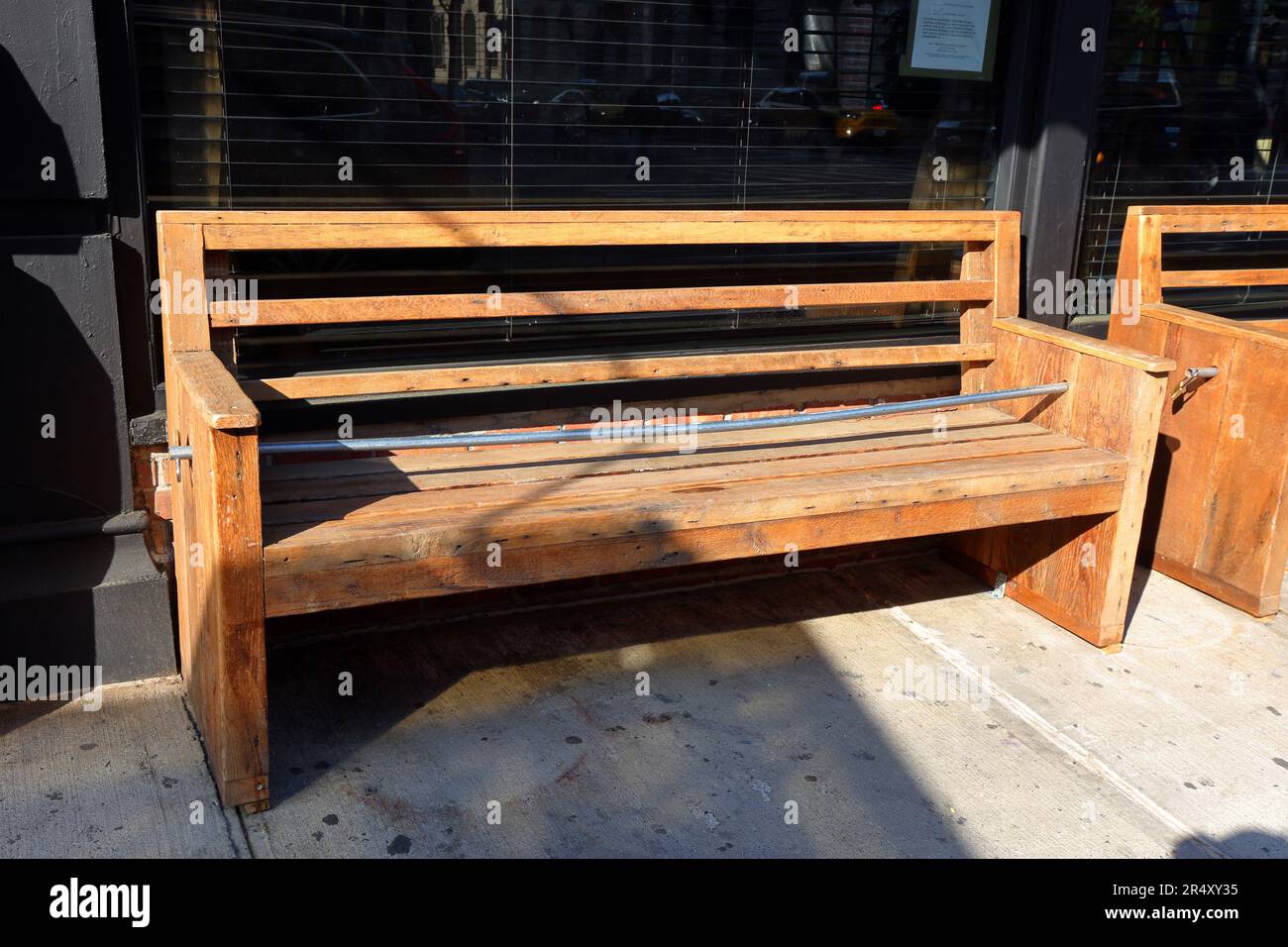 Ein elektrisches Metallrohr, das auf einer Bank platziert wird, um das Sitzen und Schlafen auf einer Holzbank außerhalb eines Restaurants zu verhindern. Feindliche Architektur Stockfoto