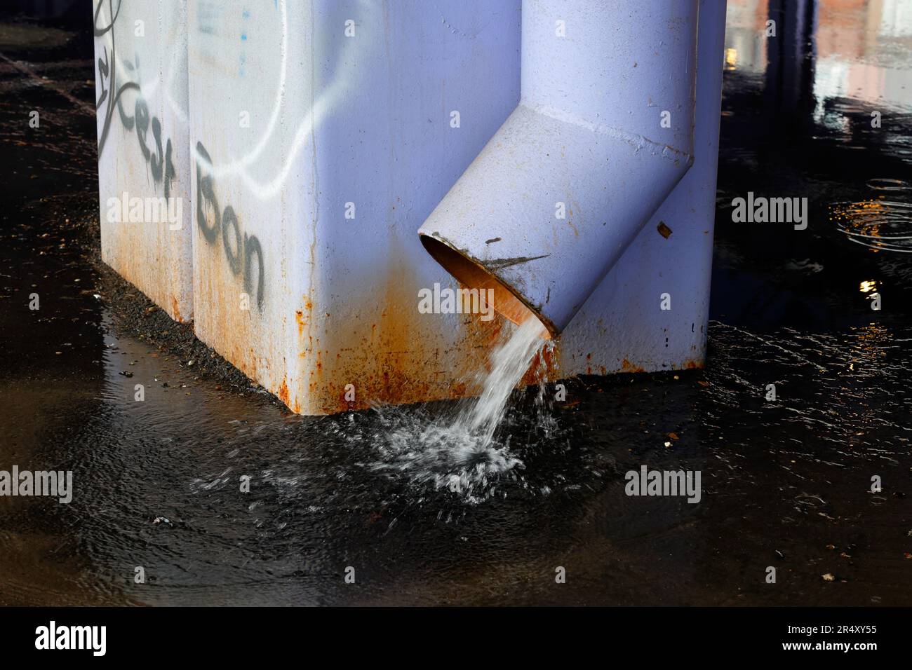 Ein Abflussrohr, das den Abfluss von nassem Wetter von einer erhöhten Autobahn in New York City leitet. Die abfließenden Pools auf den Asphaltpflaster darunter. Stockfoto