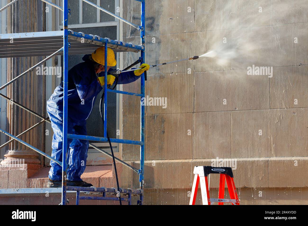 Ein Arbeiter wäscht Graffiti und Dreck mit einer Hochdrucksprühpistole von einem Schulgebäude in New York City. Stockfoto