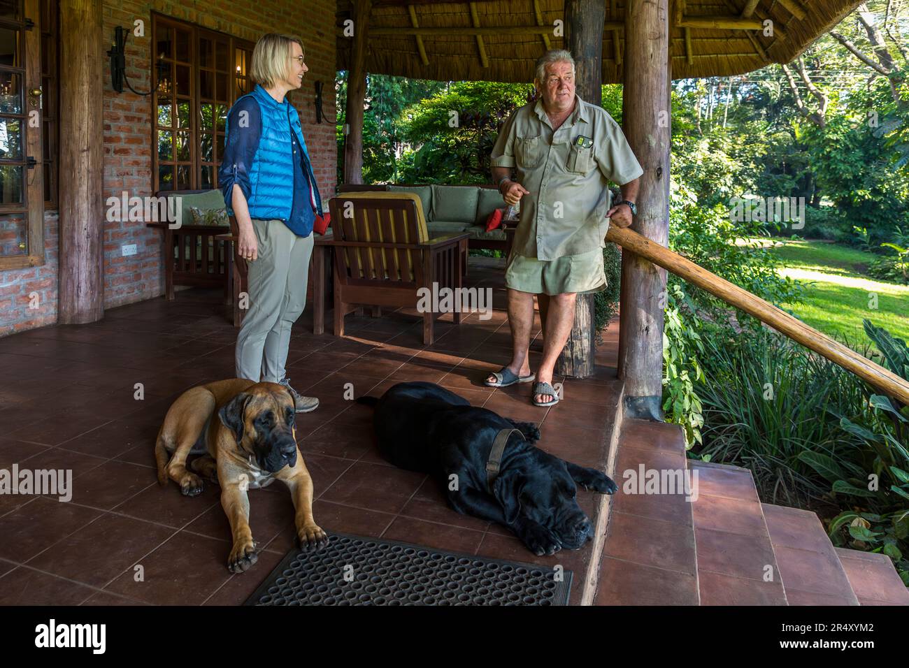 Guy Pickering, Besitzer der Kumbali Country Lodge in der Nähe von Lilongwe, Malawi, spricht mit der Reisejournalistin Angela Berg auf der Veranda seiner Lodge. Zwei Hunde ruhen zu ihren Füßen. Pickering, ursprünglich aus Südafrika, kaufte die Farm im Jahr 1991. Er und seine Frau Maureen bauten sie später zu einem landwirtschaftlichen und touristischen Unternehmen aus. Stockfoto