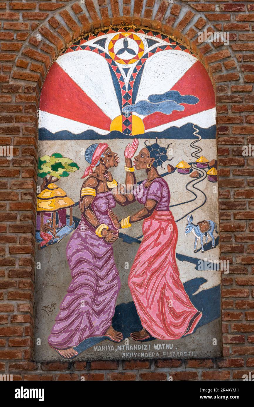 Ein Wandgemälde im Stil des Kungoni Kunst- und Kulturzentrums in Mua Mission, Malawi, stellt eine biblische Szene in afrikanischer Bildsprache dar: Marias Besuch bei Elisabeth, identifiziert durch die Chichewa-Unterschrift „Mariya, Mthandizi wathu, akuyendera Elizabeti“ („Maria, unsere Helferin, besucht Elisabeth“). Stockfoto