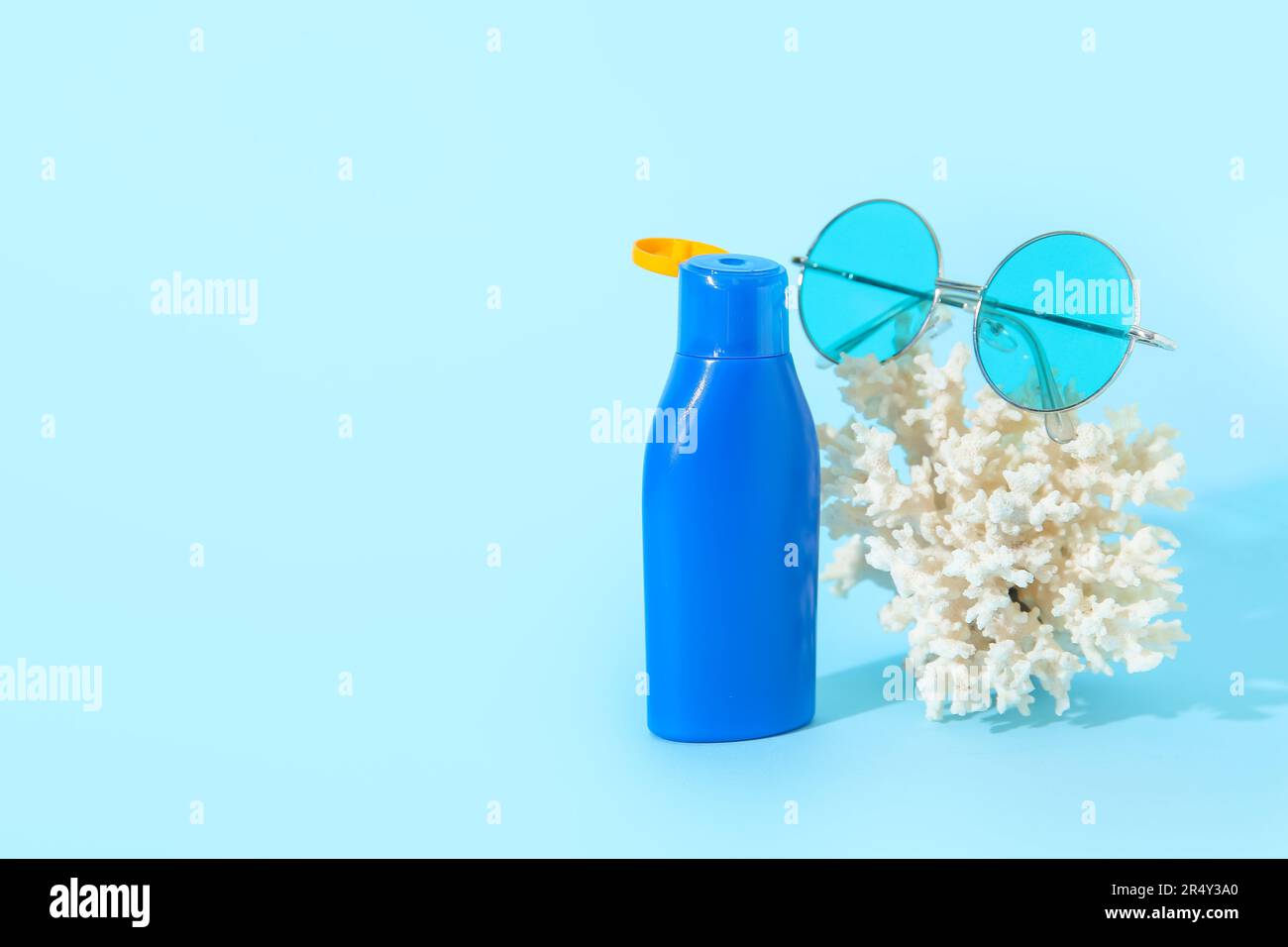 Eine Flasche Sonnencreme mit Sonnenbrille und Koralle auf blauem Hintergrund Stockfoto