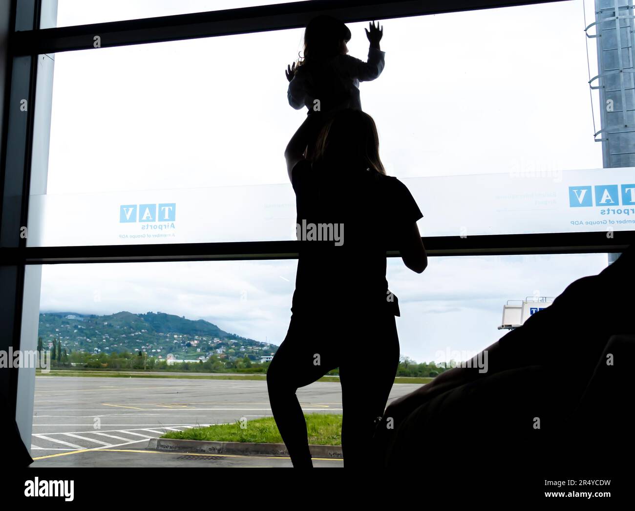 Mutter hält Baby vor dem Flughafenfenster, Silhouette. Rückansicht einer Frau, die ihrem Kind den Flugplatz zeigt. Stockfoto