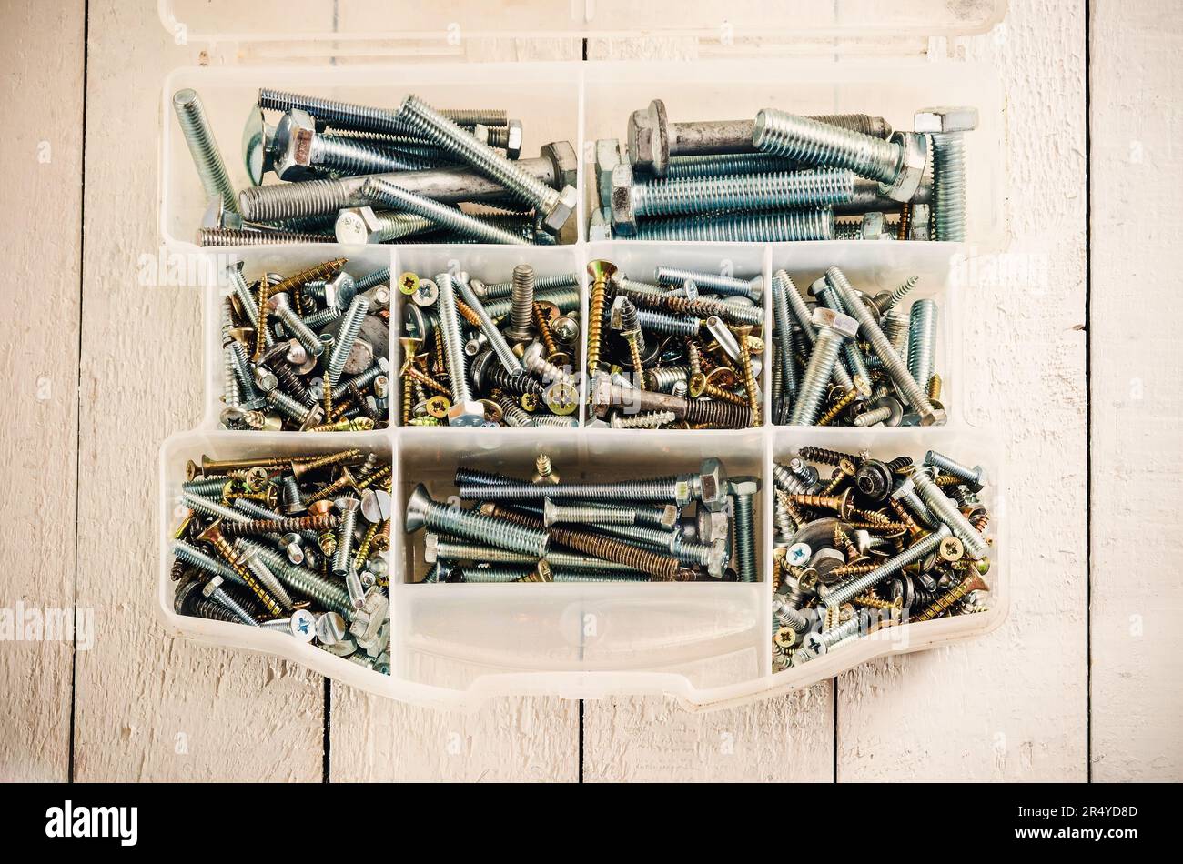 Silberne und goldene Metallschrauben. Werkzeugkasten mit Schrauben und Bolzen auf einem weißen Holztisch. Stockfoto