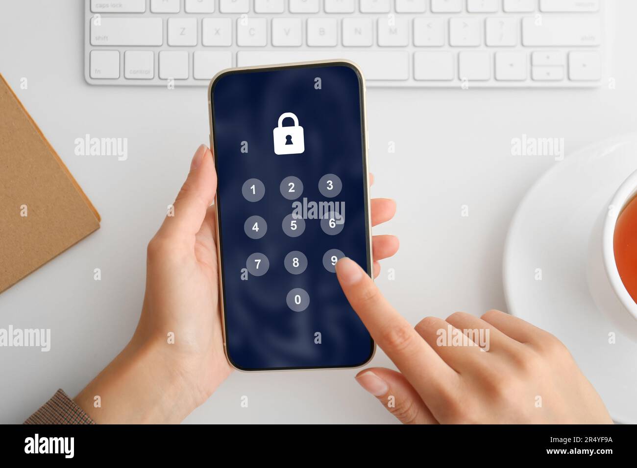 Schutz der Privatsphäre. Frau, die PIN-Code auf dem Smartphone am weißen Tisch eingibt, Draufsicht. Sperren und Nummernfeld auf dem Bildschirm Stockfoto