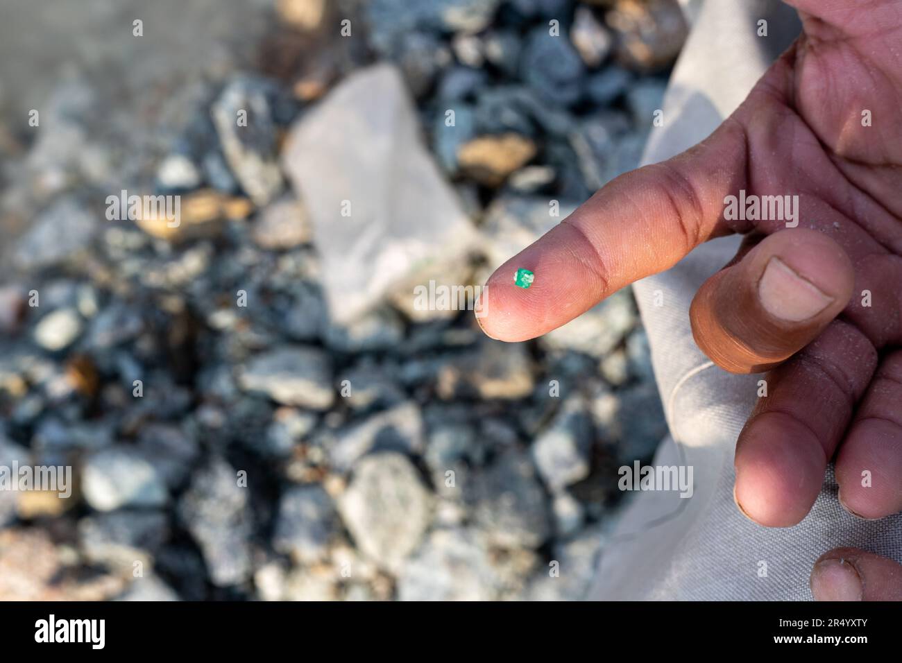 Ein Mann, der ein kleines Stück Smaragdstein an seiner Fingerspitze zeigt. Selektiver Fokus mit unscharfem Hintergrund Stockfoto