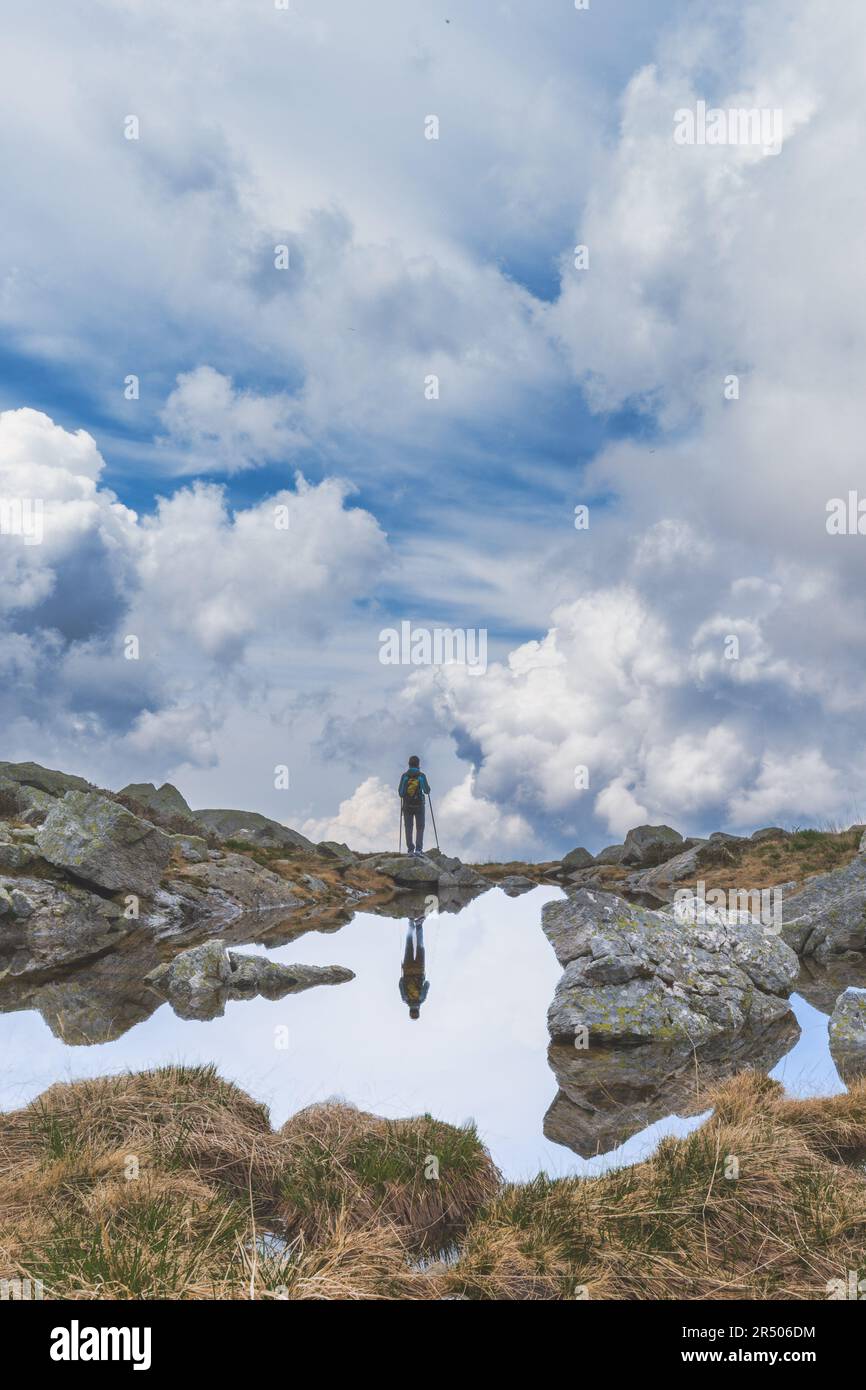 Eine entfernte Person beobachtet den Himmel in der Nähe eines kleinen Bergsees Stockfoto