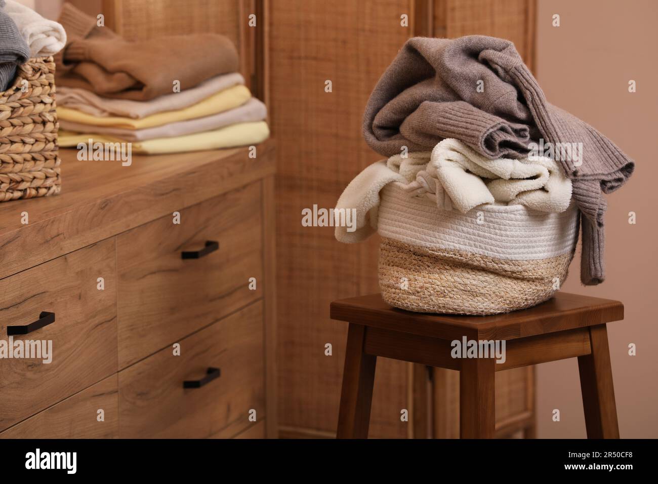 Korb mit Korbwäscherei überfüllt mit Kleidung auf Holzhocker im Innenbereich Stockfoto