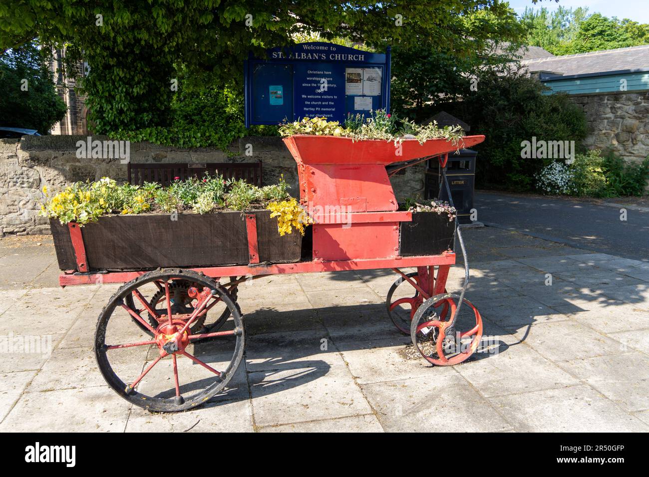 Earsdon, North Tyneside, Großbritannien. Alte Landmaschinen, die als Pflanzmaschine vor der St. Alban's Kirche wiederverwendet wurden. Stockfoto