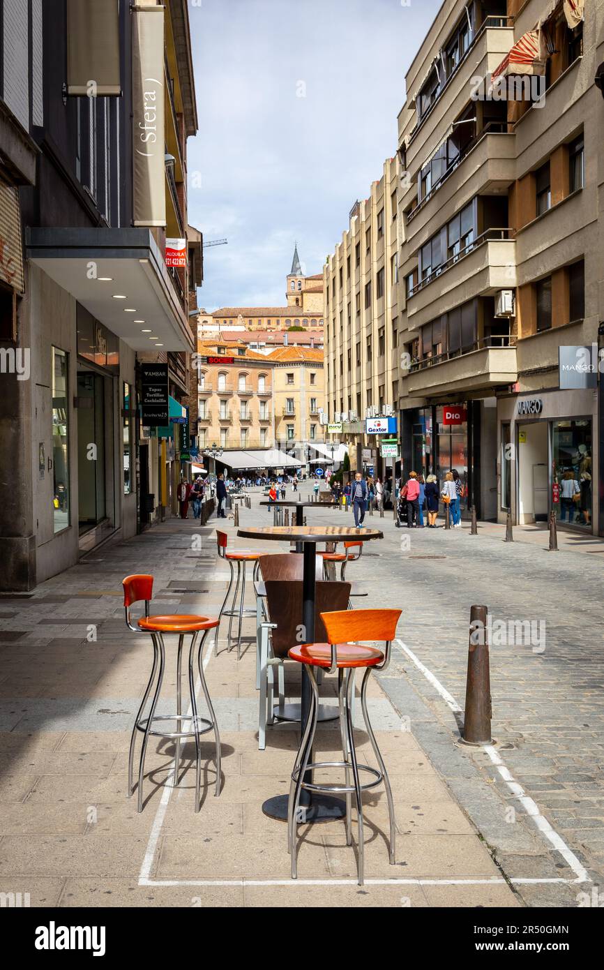 Segovia, Spanien, 03.10.21. Café- und Restauranttisch mit Stühlen in einer schmalen mittelalterlichen Stadtstraße von Segovia mit Menschen, die zu Fuß gehen. Stockfoto