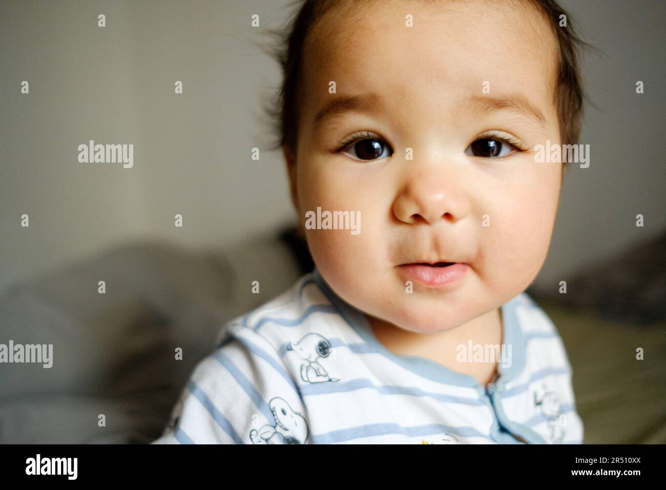 Nahaufnahme eines lateinamerikanischen Babys, das im Schlafzimmer lächelt, mit weichem, natürlichem Licht, das in die Kamera schaut. Süßes hispanisches Mädchen Stockfoto