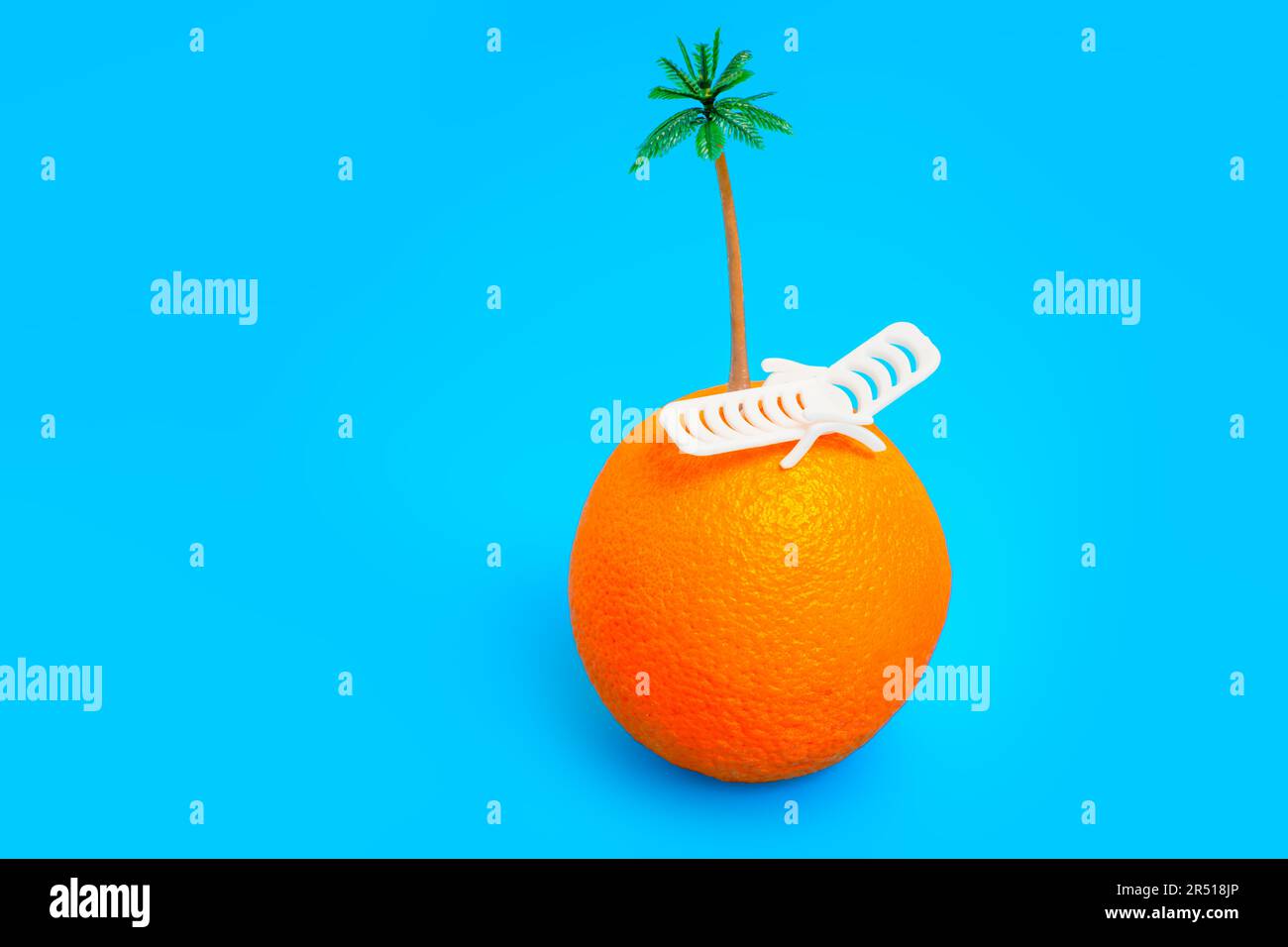 Orangenfrucht mit Miniaturliege und Palmenspielzeug oben isoliert auf blauem Hintergrund. Tropenurlaub, Konzept für exotische Reiseziele. Stockfoto