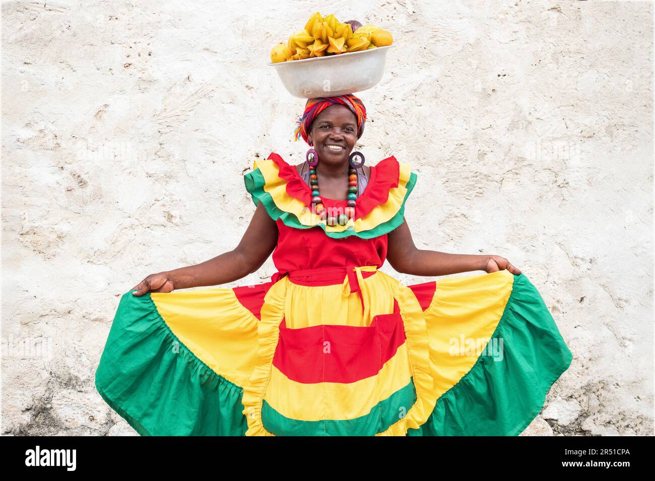 Fröhlicher Straßenverkäufer mit frischem Obst, auch bekannt als Palenquera, in der Altstadt von Cartagena de Indias, Kolumbien. Afro-kolumbianische Frau in traditioneller Kleidung. Stockfoto