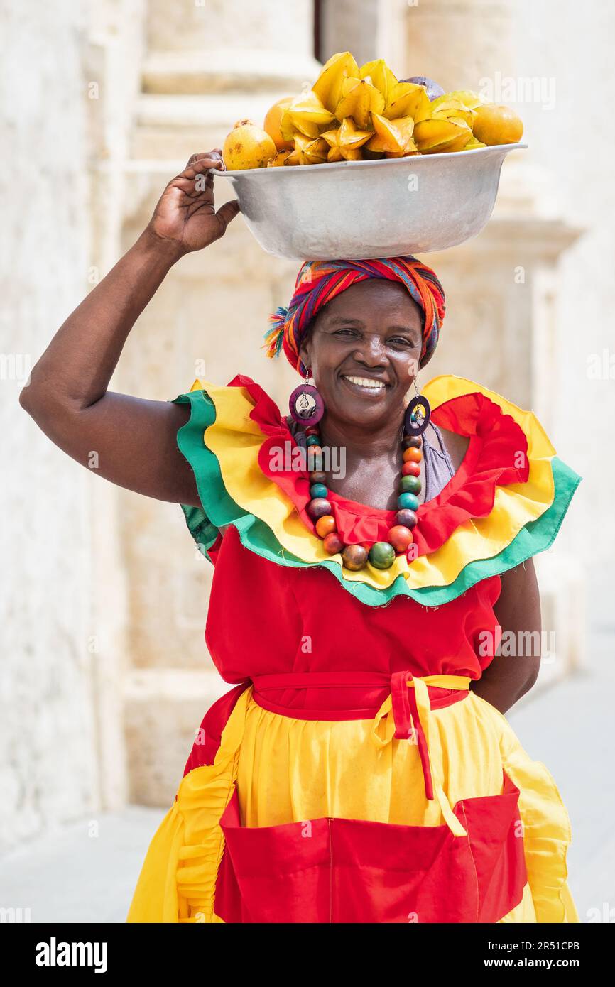 Fröhlicher Straßenverkäufer mit frischem Obst, auch bekannt als Palenquera, in der Altstadt von Cartagena de Indias, Kolumbien. Afro-kolumbianische Frau in traditioneller Kleidung. Stockfoto